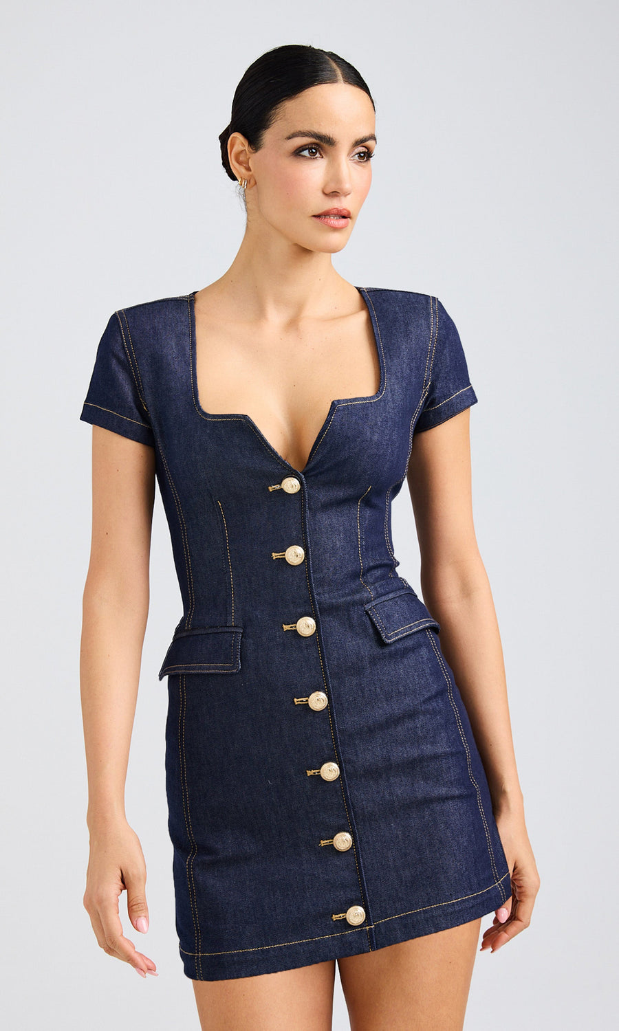 A dark hair model wearing a dark denim dress featuring gold buttons, presenting a chic and trendy appearance.