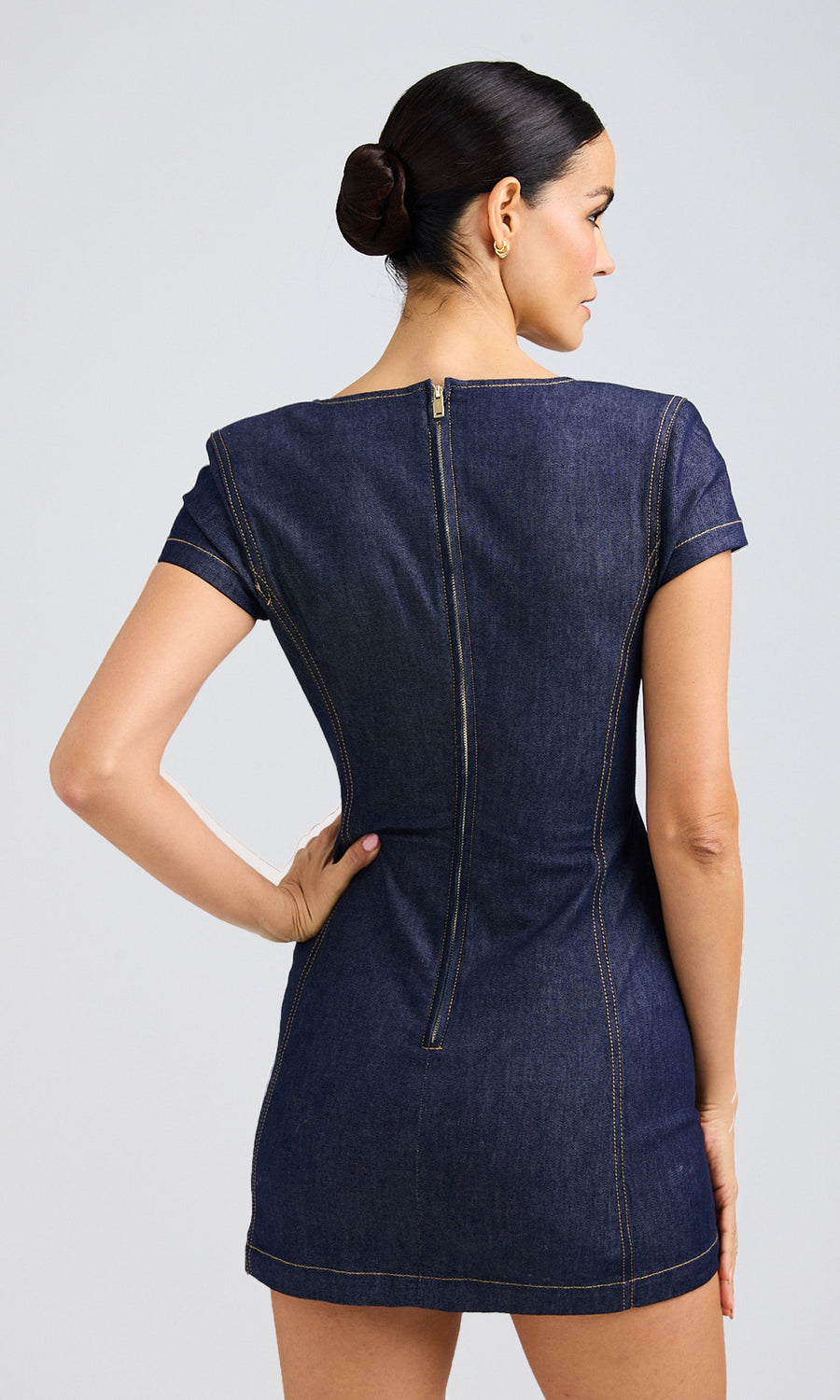 Rear view of a woman in a dark denim dress, highlighting the zipper on her back as she poses confidently.