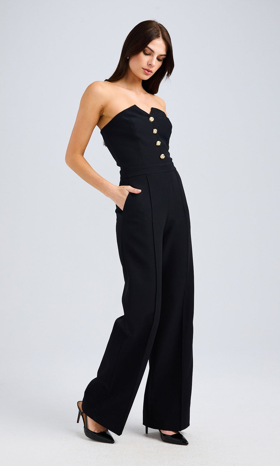 Side angle of the model wearing the black jumpsuit, highlighting the gold-button detail and tailored fit.