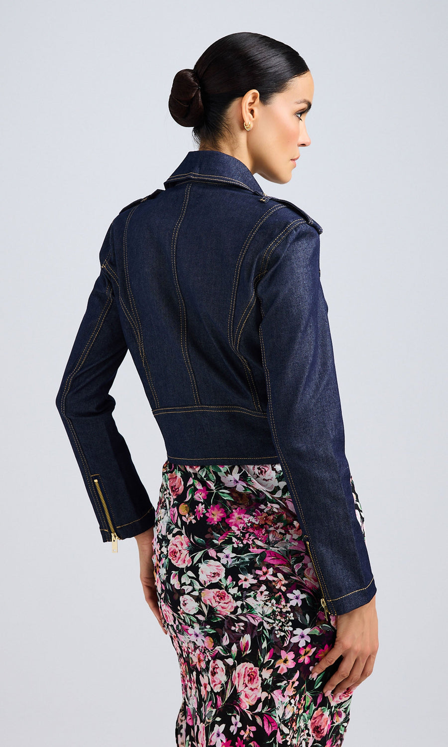 Back view of a woman in a dark denim jacket and a floral skirt, highlighting her trendy fashion choice.