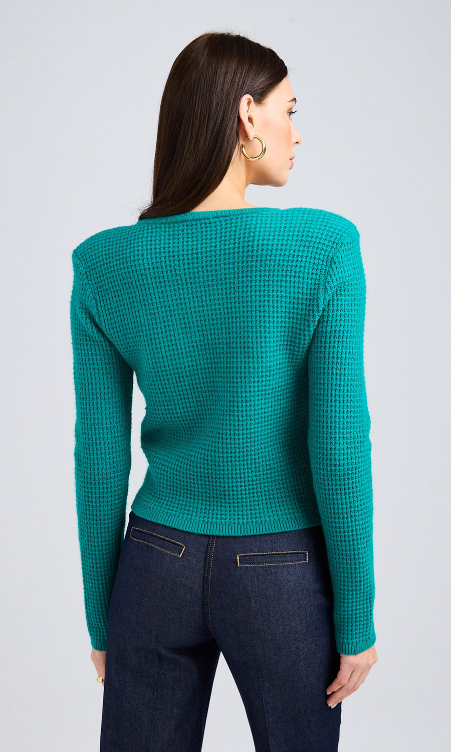 Rear-view of woman wearing a waffle-knit sweater in Topaz paired with dark wash jeans.