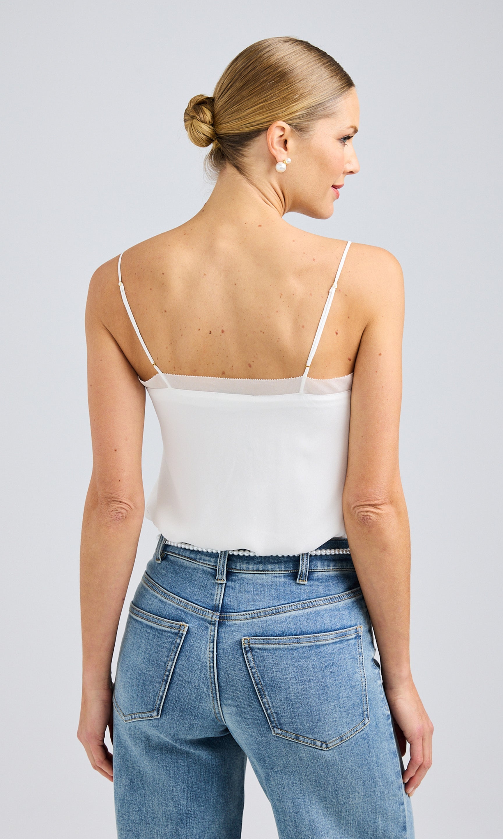 Rear view of a white cami with thin straps and a relaxed fit, styled with light blue denim jeans featuring classic stitching