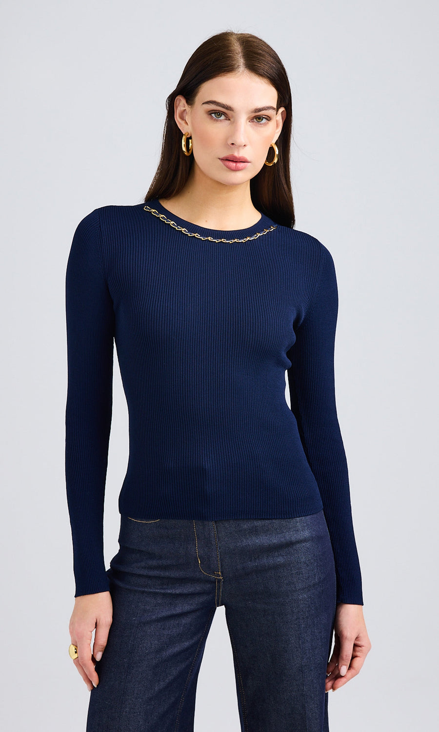 Model standing wearing blue sweater with chain around neck