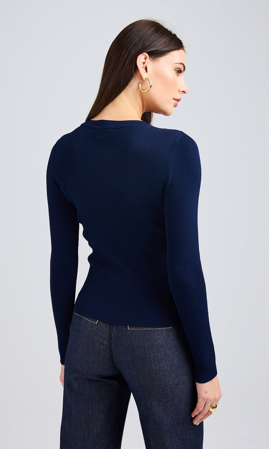 Back view of model standing wearing blue sweater with chain around neck