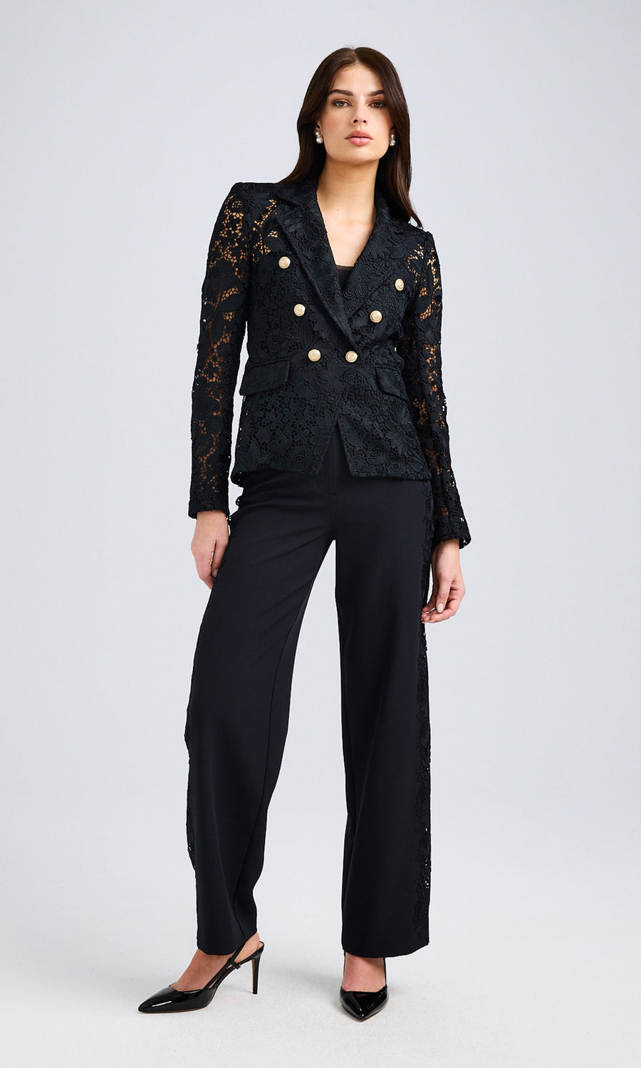 Full-body front view of the model showcasing the black lace blazer paired with tailored black trousers and pointed heels.