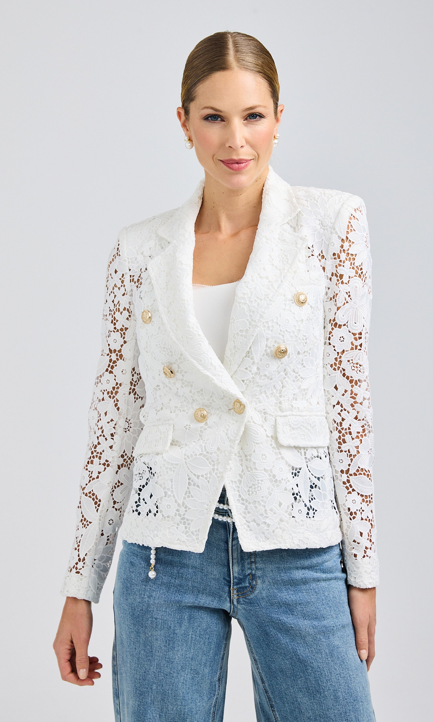 Front view of the model wearing a white lace blazer with gold button accents, styled with light-wash denim jeans.