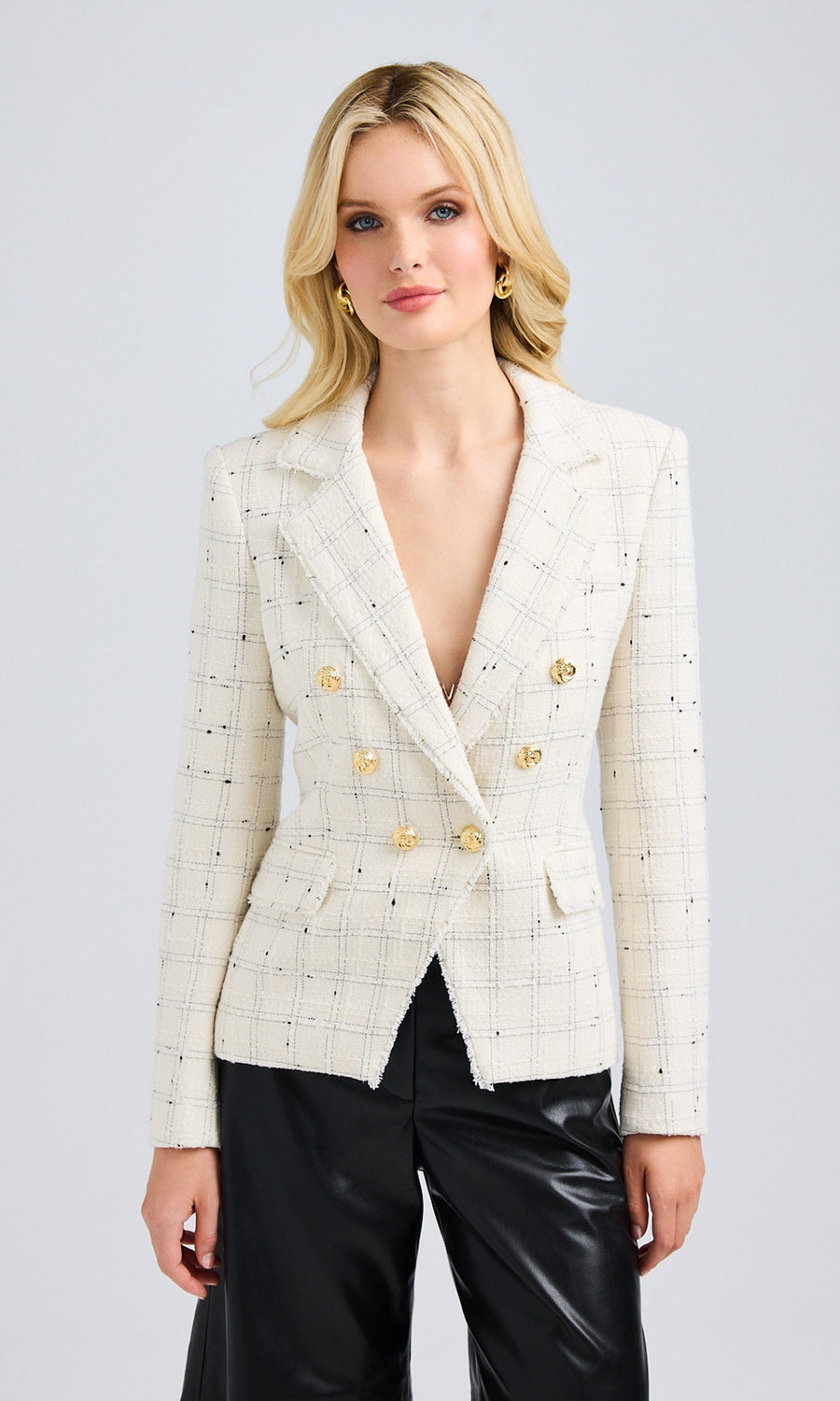 Model wearing a tailored white tweed jacket styled with black leather pants, showcasing the fitted silhouette and gold knot buttons.