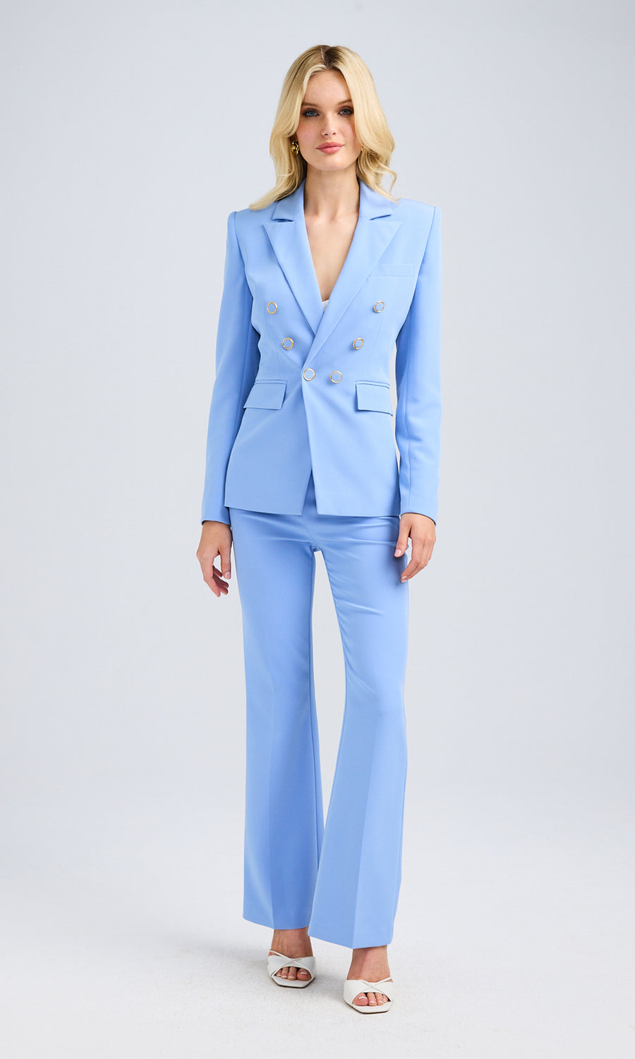 A woman in a blue blazer with gold buttons and high heels stands confidently, showcasing her stylish outfit.