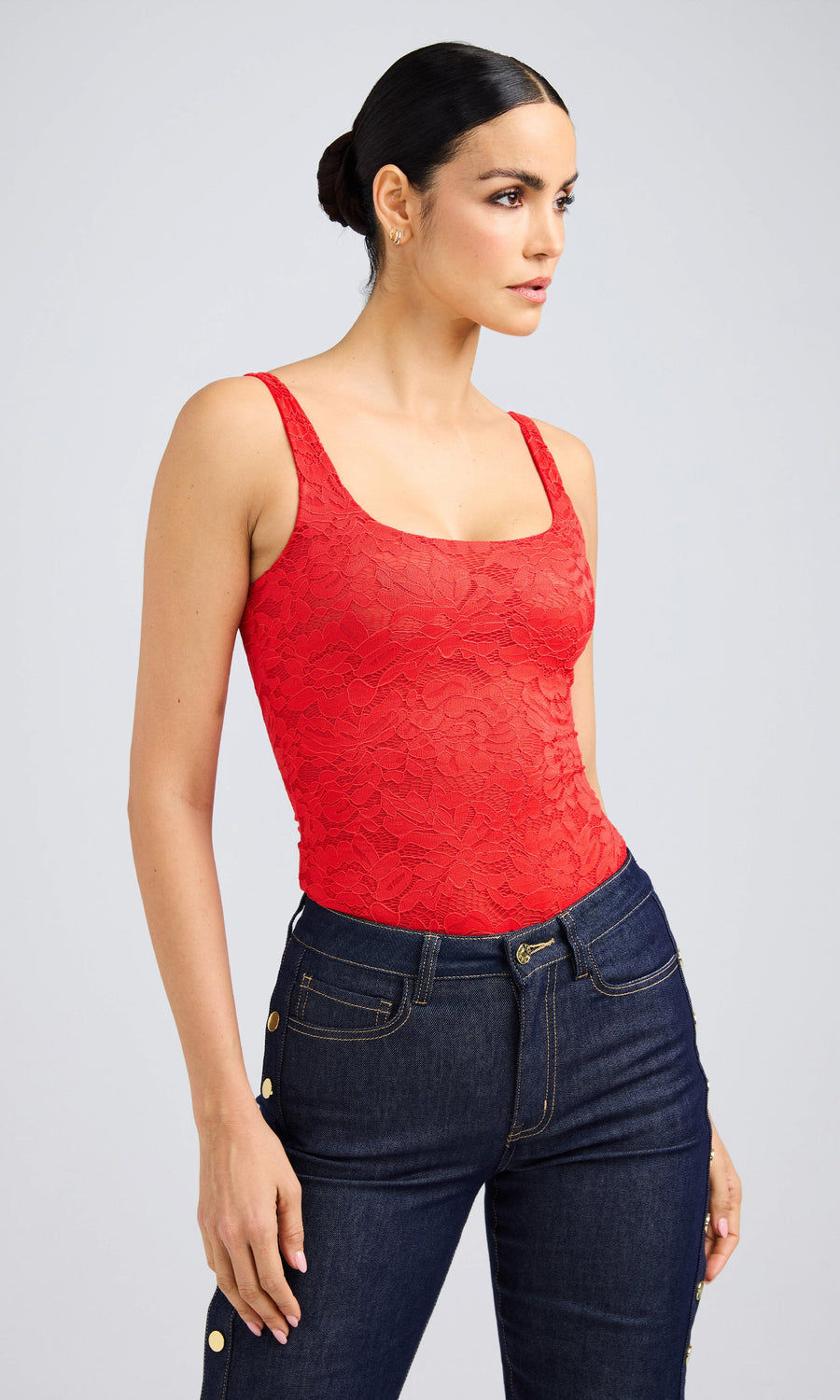 A woman in a red lace bodysuit and jeans, glancing sideways, showcasing her stylish outfit