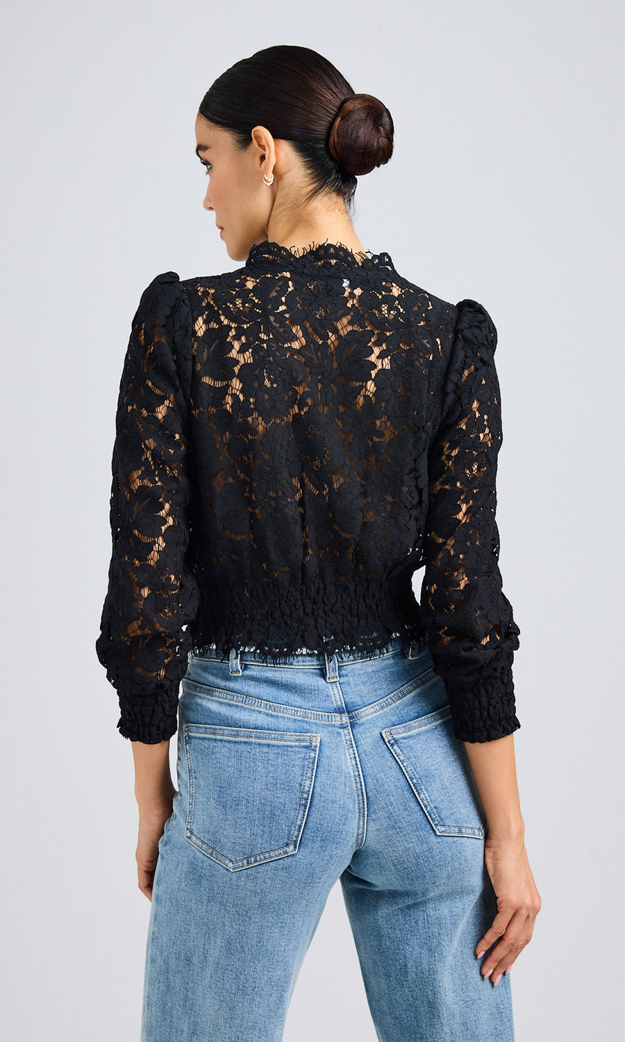 Rear-view of a woman wearing a long-sleeve black blouse with sheer lace details and light jeans.