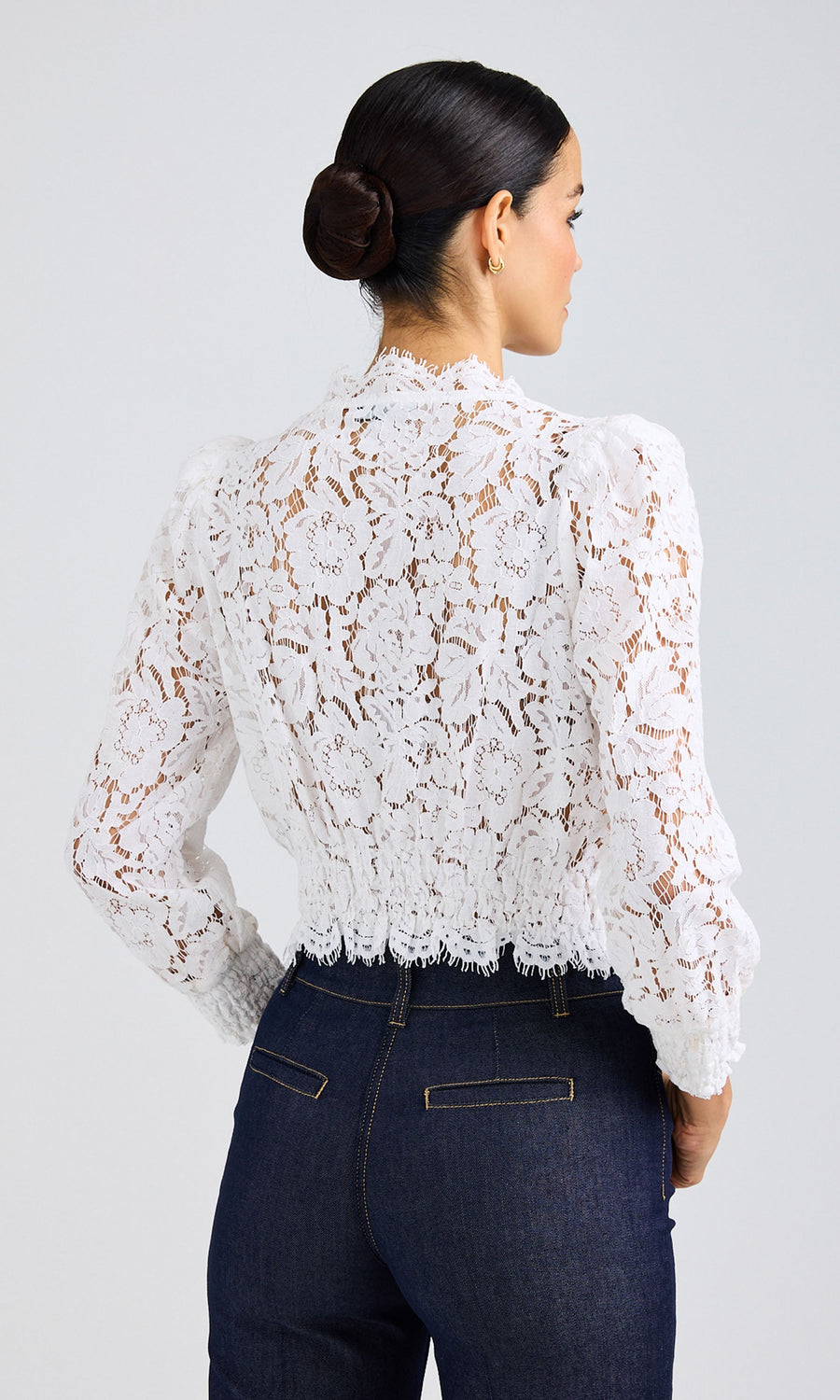 Rear view of woman wearing a sheer/white lace blouse with long sleeves and dark jeans.