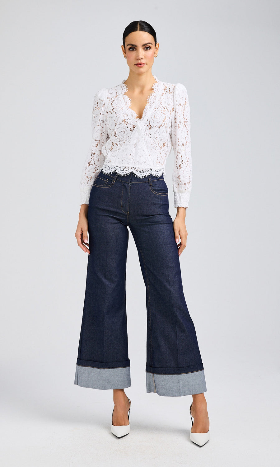 Woman wearing dark-washed, wide-leg jeans paired with a white, deep v-neck lace blouse.