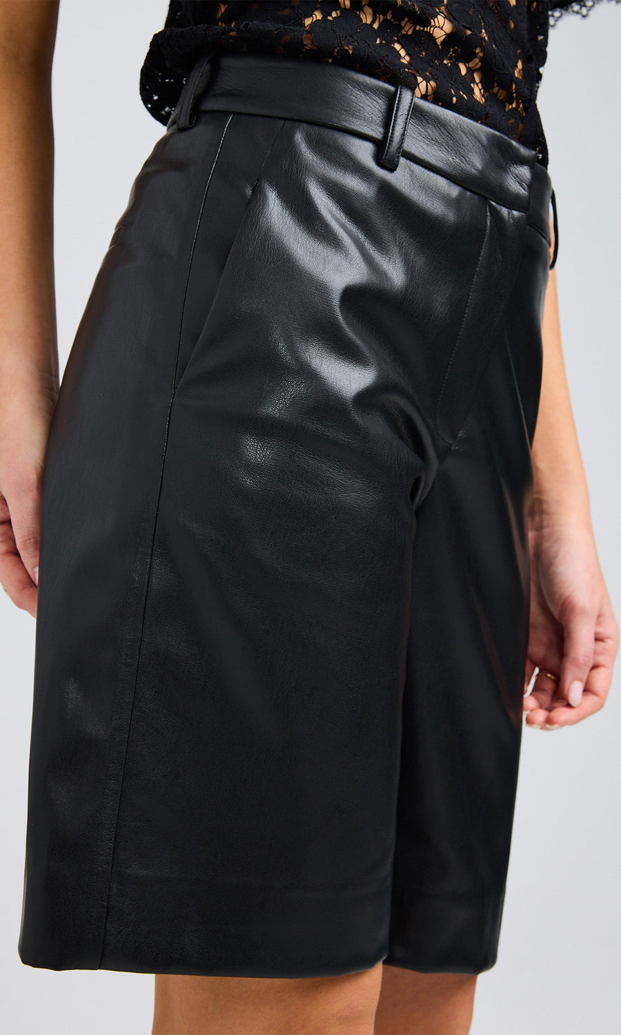 Close-up of the black vegan leather bermuda shorts, highlighting the smooth texture and functional pocket details.