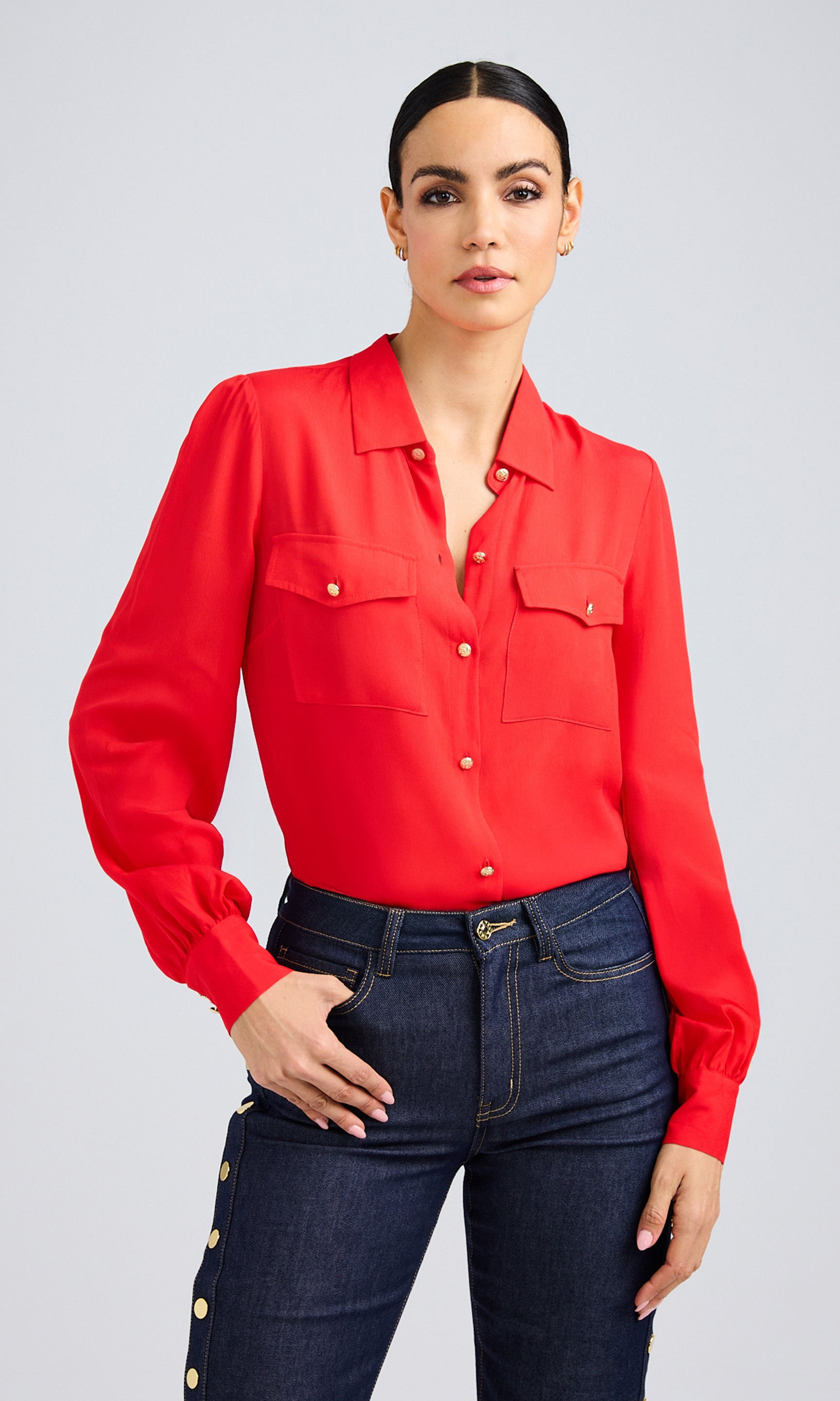 Model wearing a vibrant flame red blouse with long sleeves and front patch pockets, styled with dark denim snap-button pants.