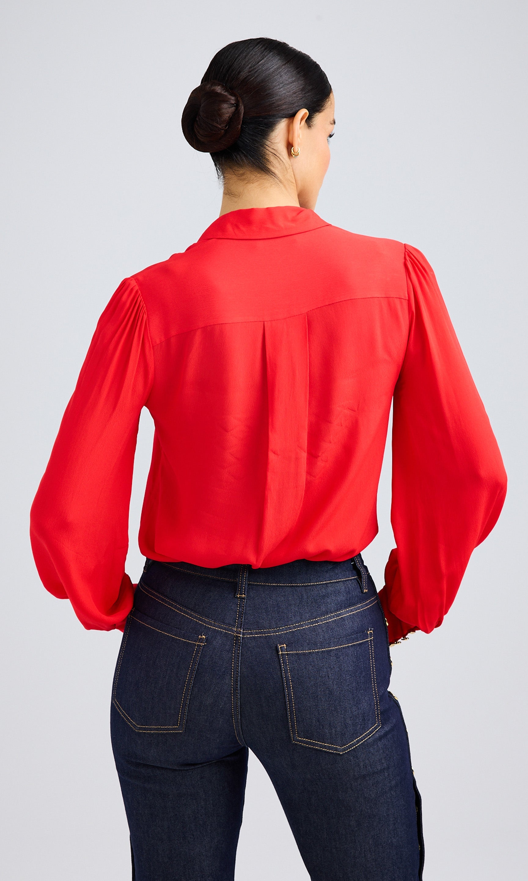 Back view of a flame red blouse showcasing the soft pleats and relaxed fit, paired with dark denim pants.