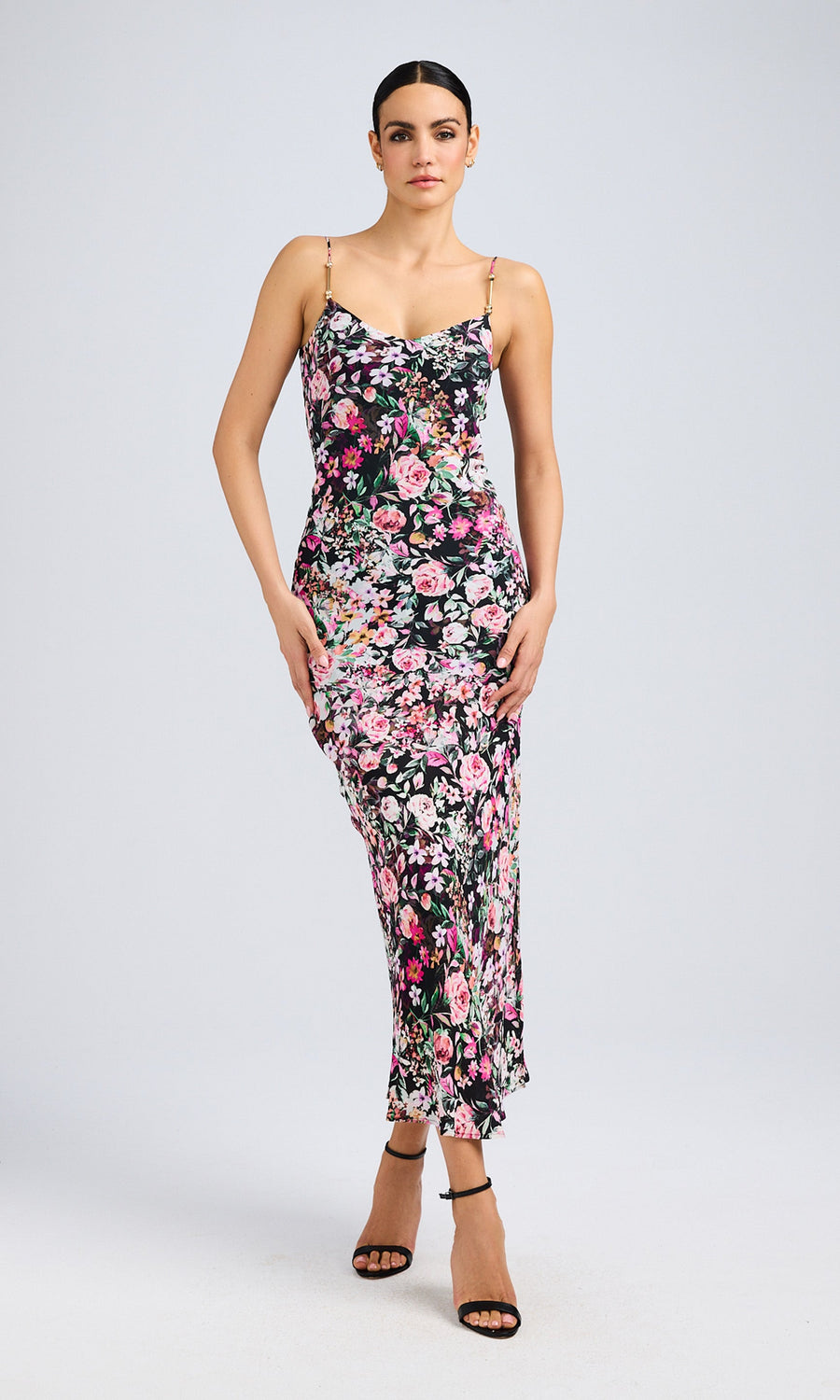 Model wearing a floral midi dress with spaghetti straps and a fitted silhouette, standing confidently in heels.