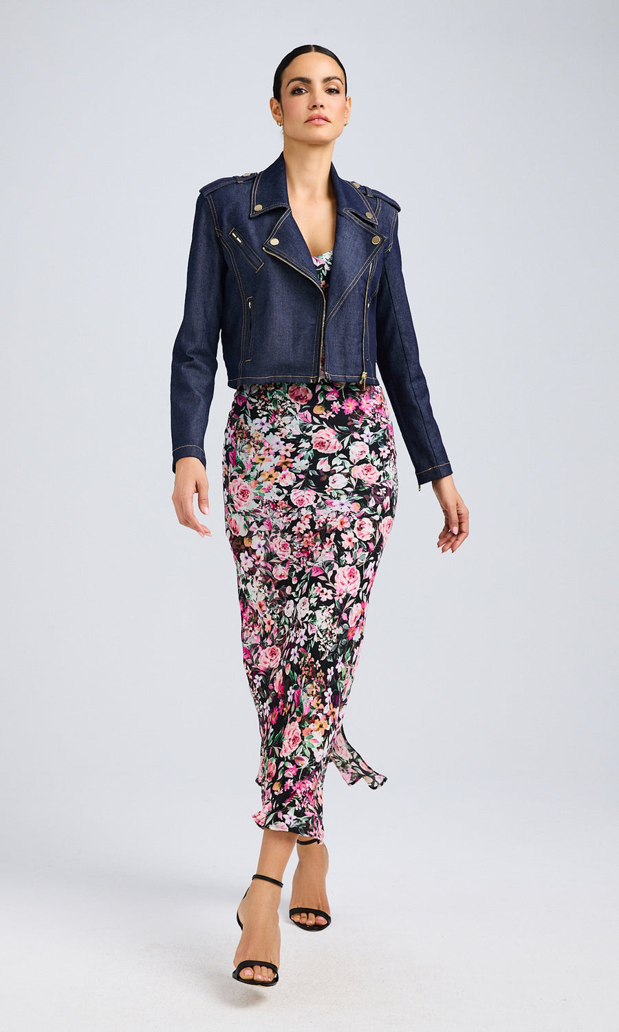 Model in a dark denim moto jacket and a floral skirt stands tall, displaying her trendy and vibrant style.