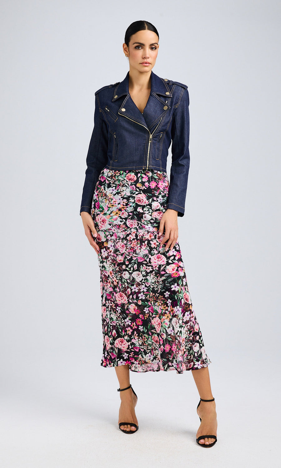 The outfit features a floral midi skirt, dark denim jacket, and black heels for a chic, modern look.