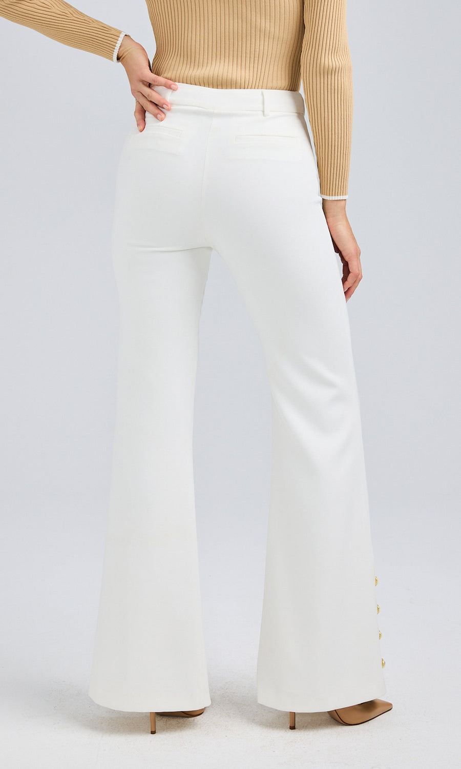 Rear angle of white crepe pants, showcasing a tailored fit with back pocket details and a flared silhouette. Styled with a beige ribbed cardigan.