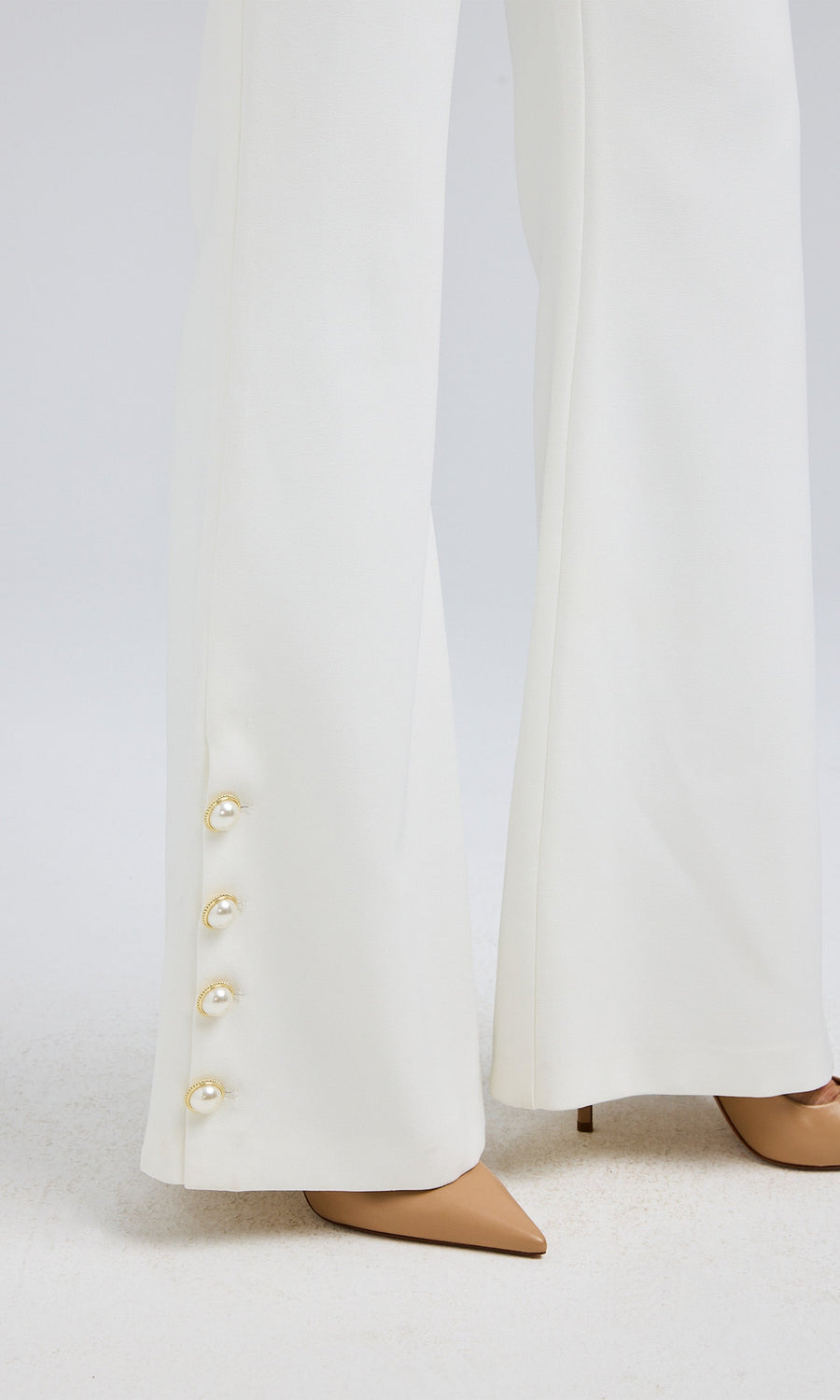 Close-up view of white crepe pants, focusing on the luxurious gold and pearl button.