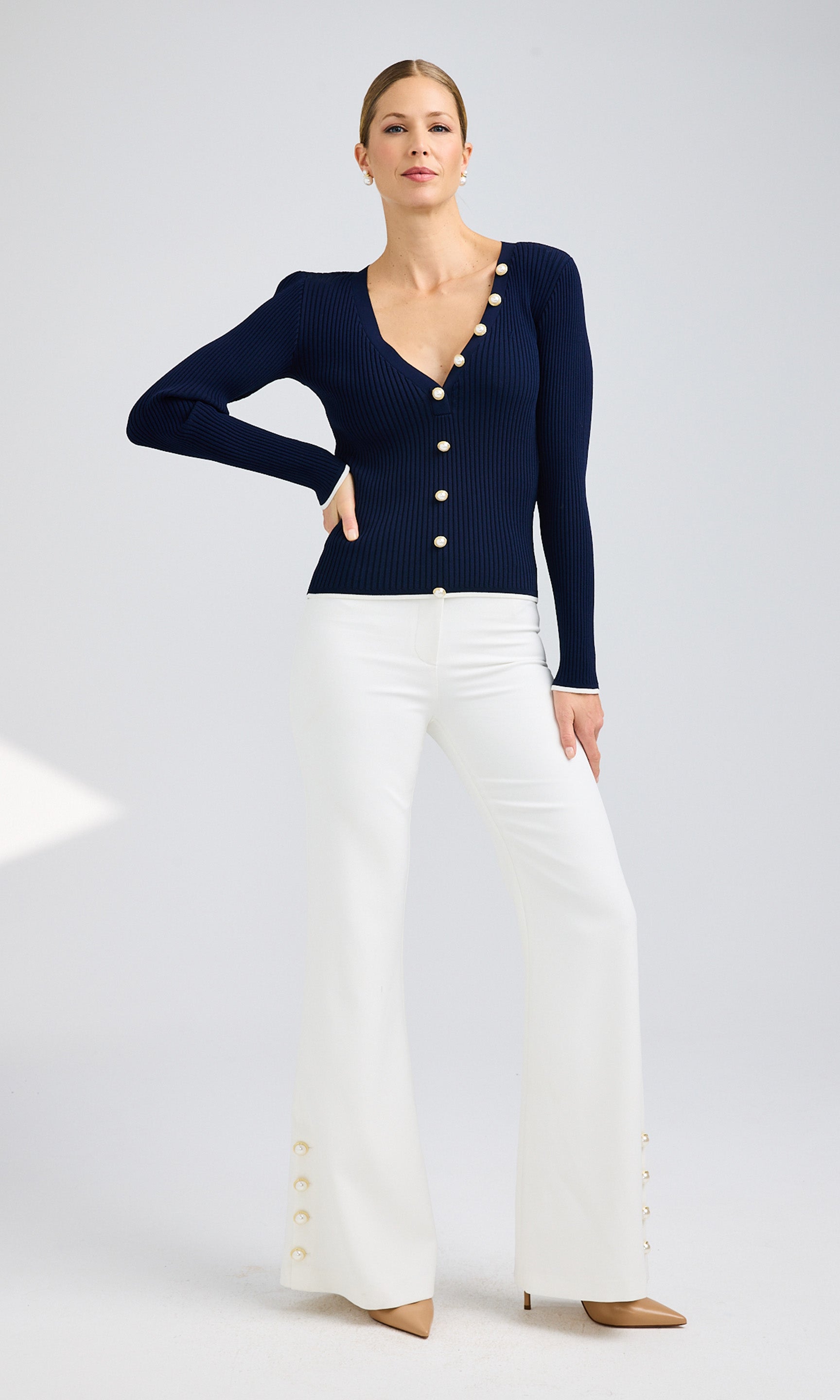 Full-body view of a model wearing a navy cardigan with pearl buttons and white pants, exuding a chic style.