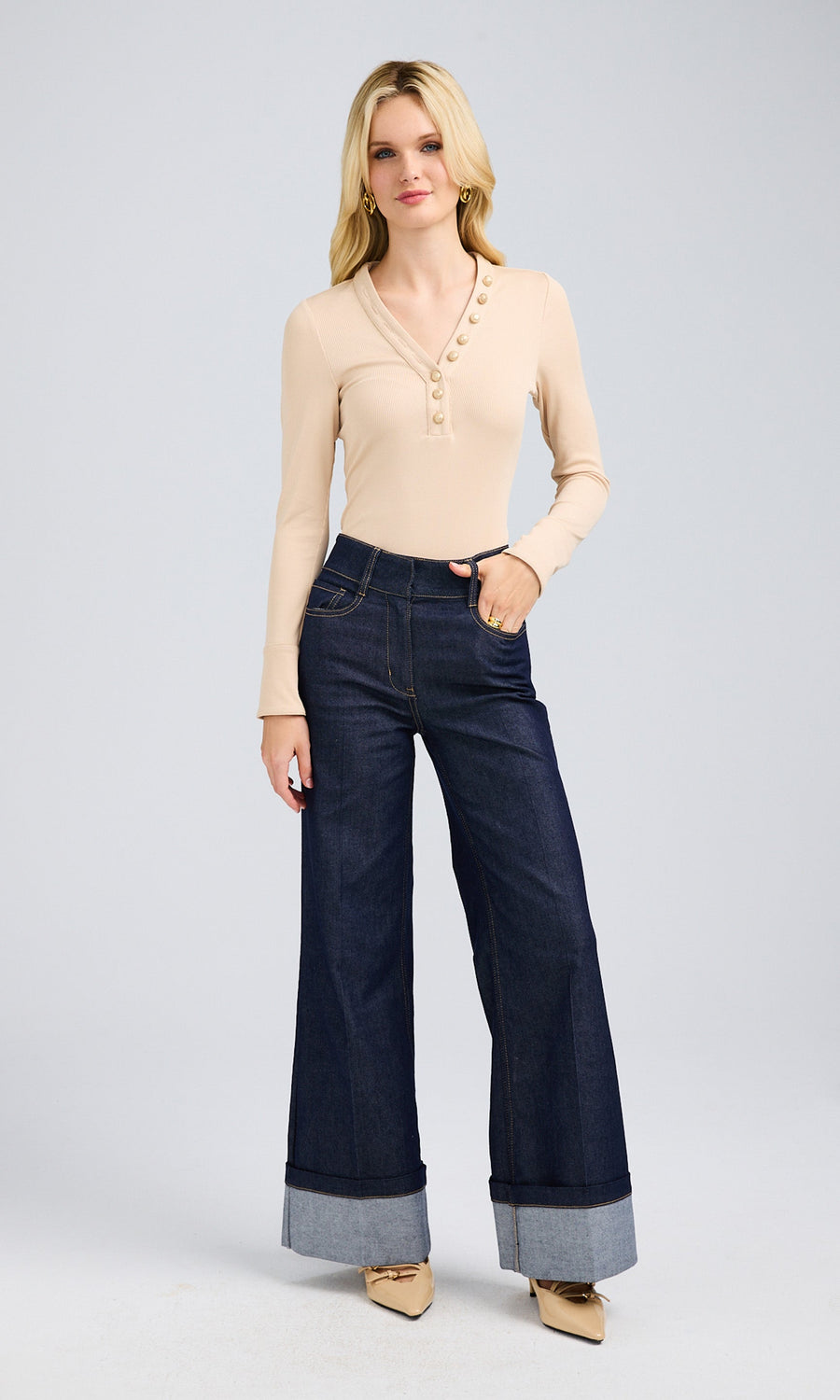 Woman wearing a fitted long-sleeve top with a ribbed texture and high-waisted dark blue jeans.