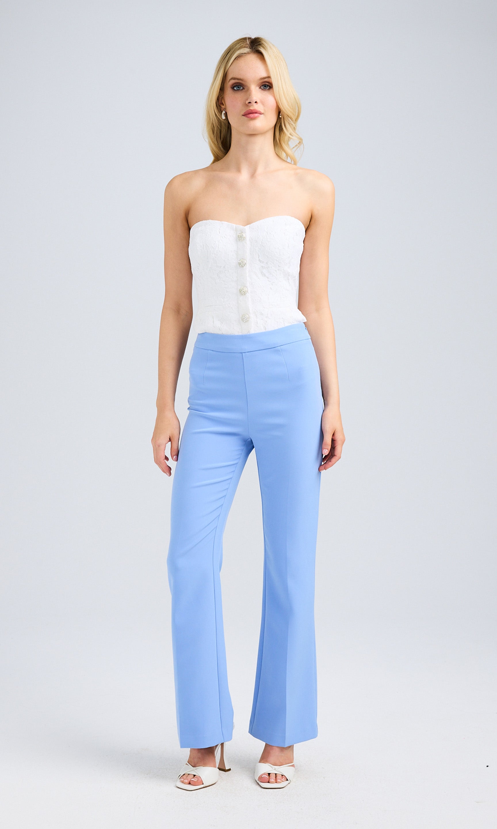 Blonde model dressed in blue crepe pants and a white top, exuding a chic and modern look.