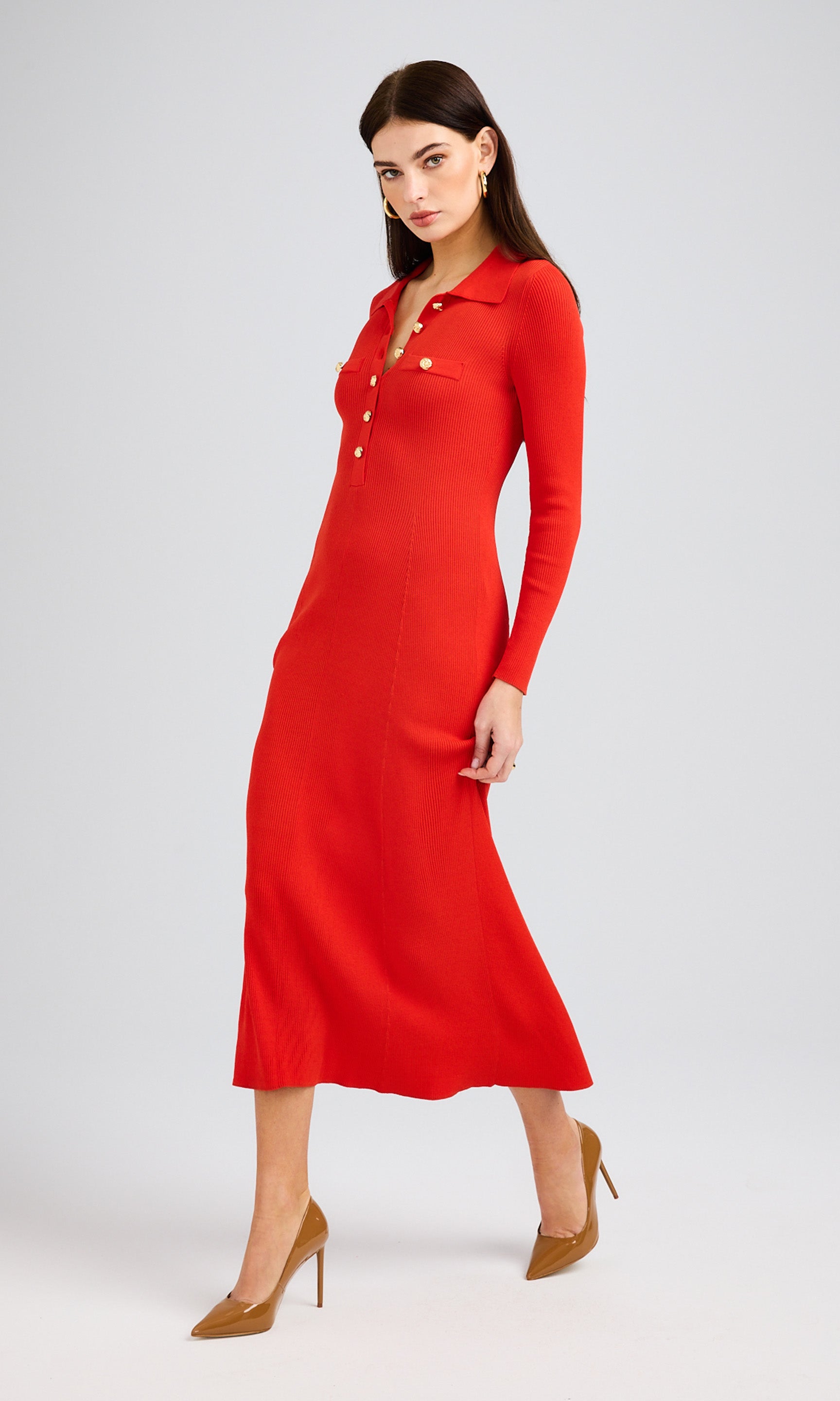 Model walks in a flame-colored sweater dress made of soft knit, featuring stylish gold buttons.