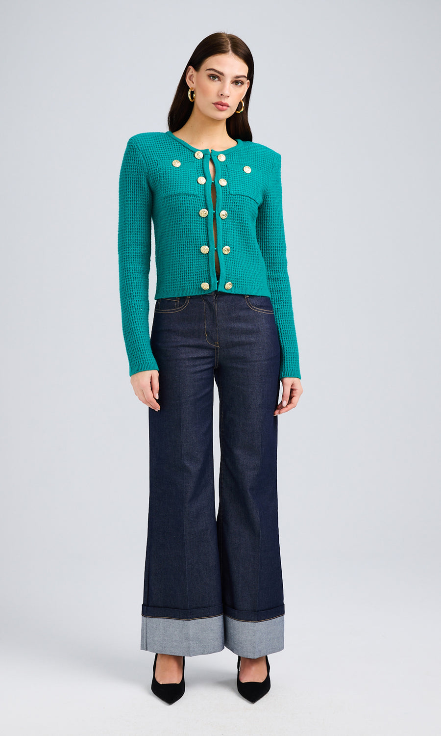 Woman wearing a topaz sweater with gold button details paired with wide-leg sheen denim jeans.