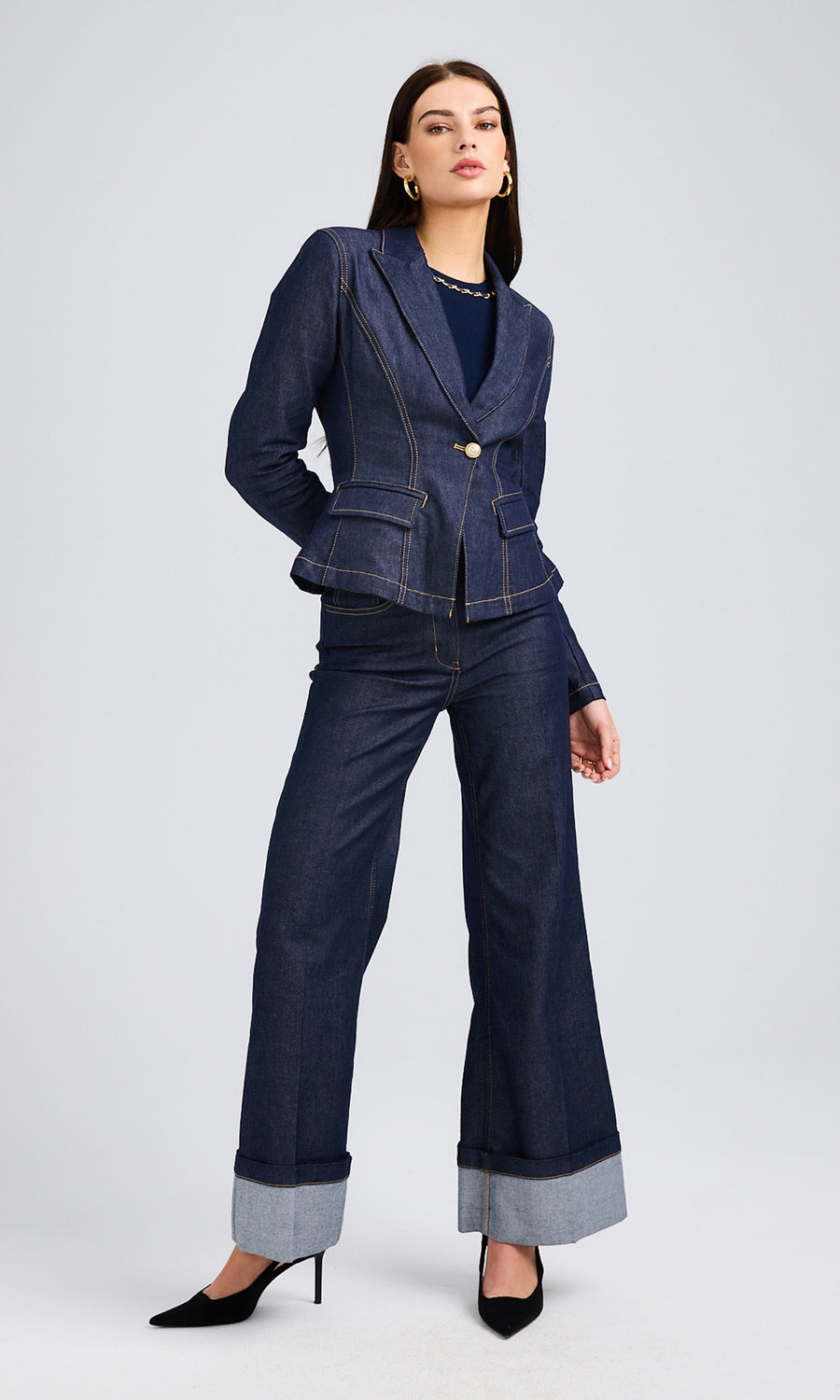 Woman in a dark denim jacket with contrasting stitching, wide-leg trousers, and black high heels.