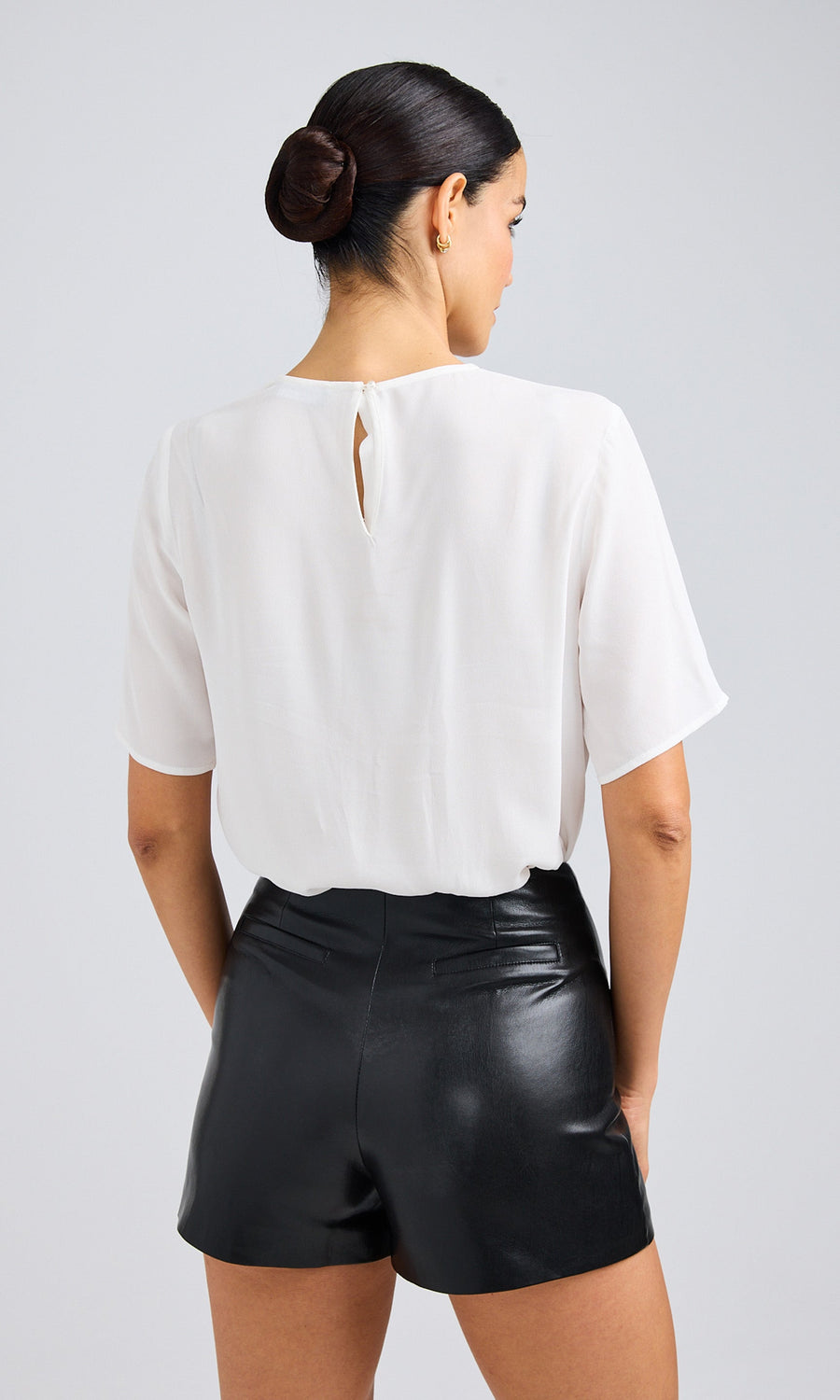 Rear view of woman wearing a white, vegan silk blouse paired with black vegan leather shorts.