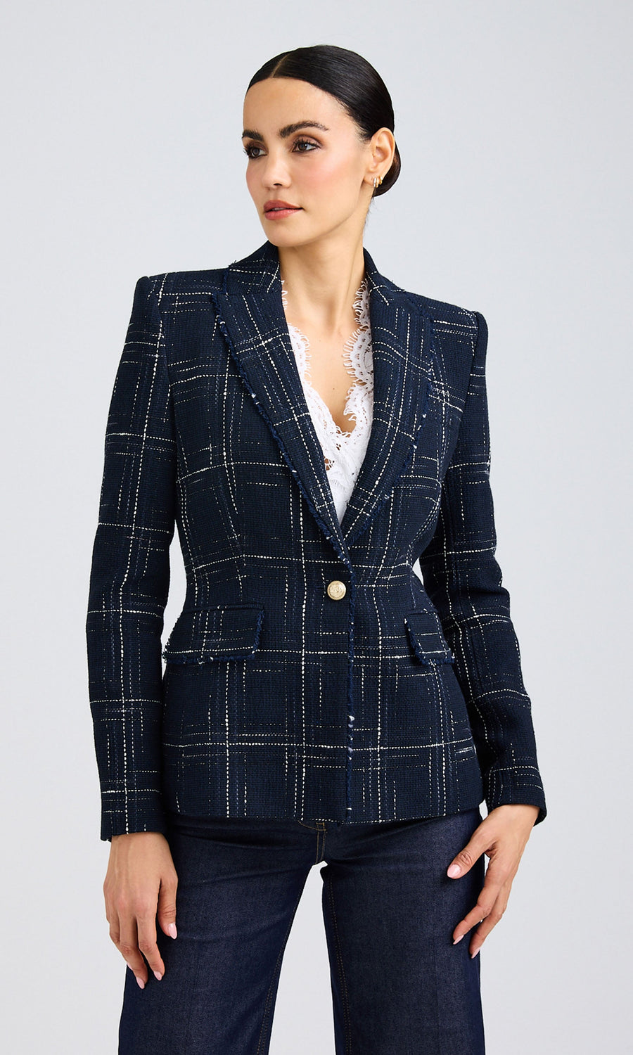 Dark-haired woman wearing a windowpane tweed blazer over a white lace blouse paired with dark jeans.