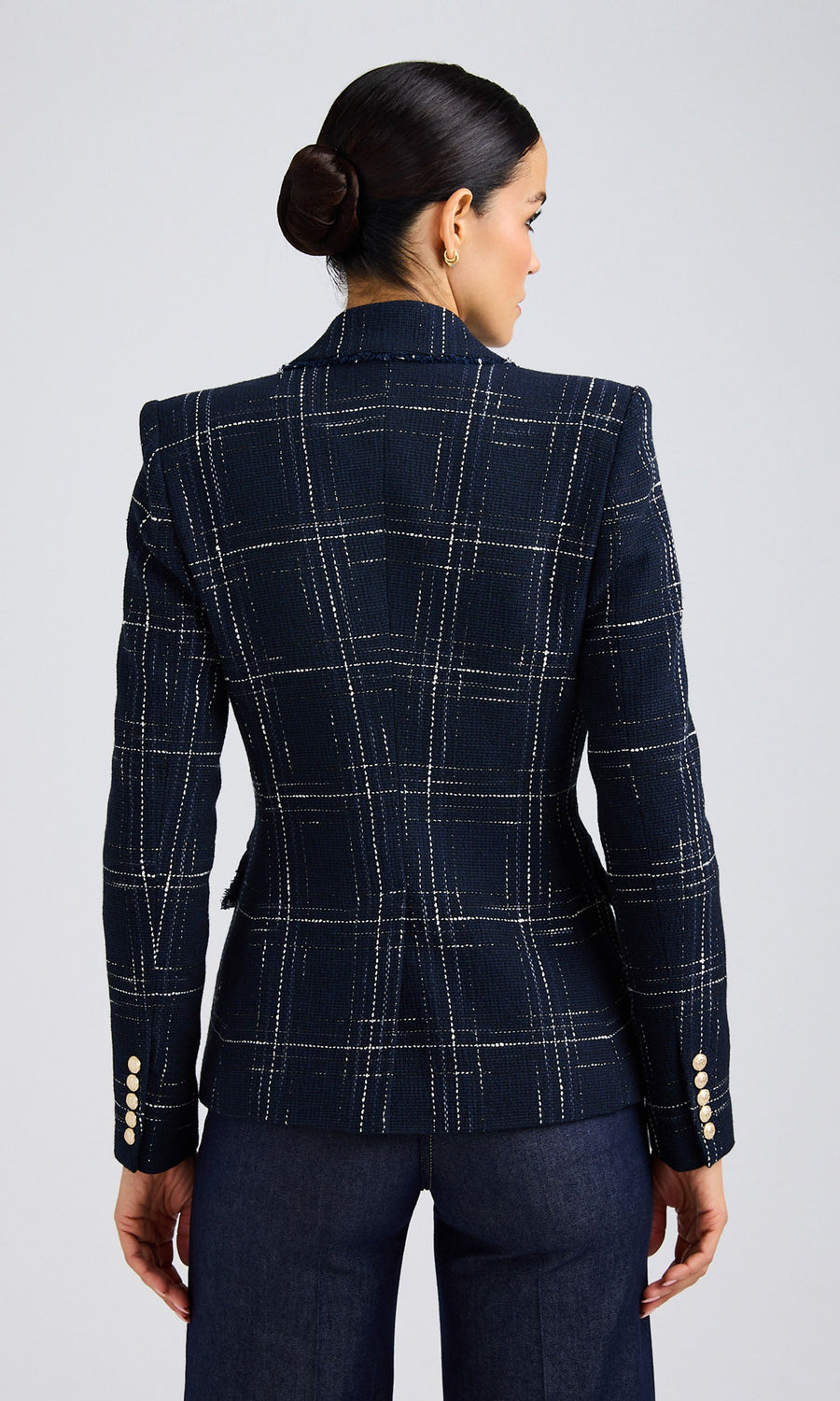 Rear-view of woman wearing a navy windowpane tweed blazer with strong shoulders and a fray trim.