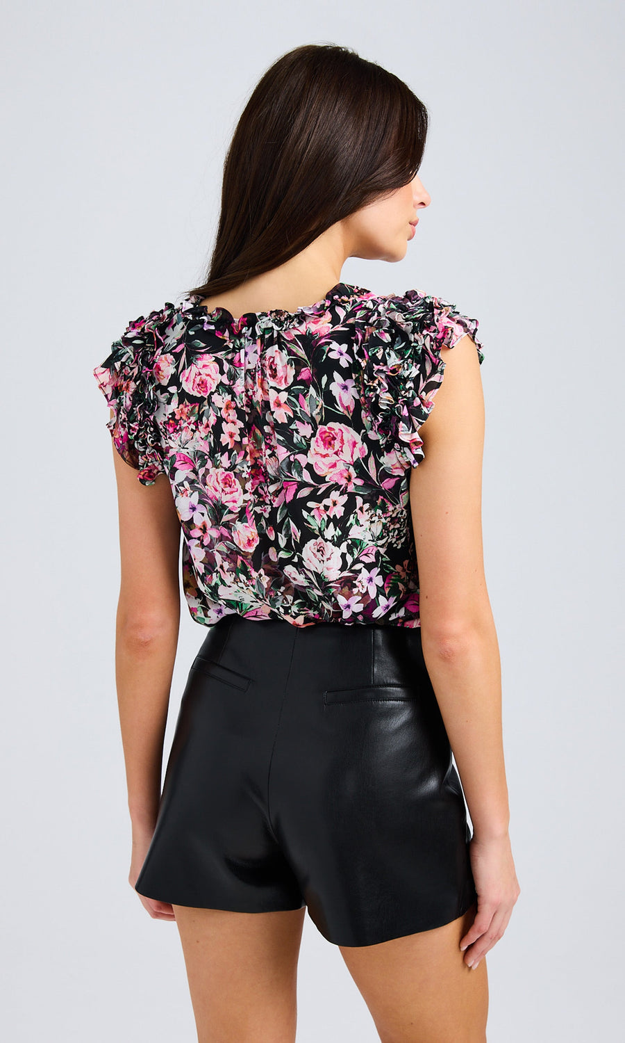 Rear view of the model showcasing a floral blouse with ruffled details, paired with black vegan leather shorts.