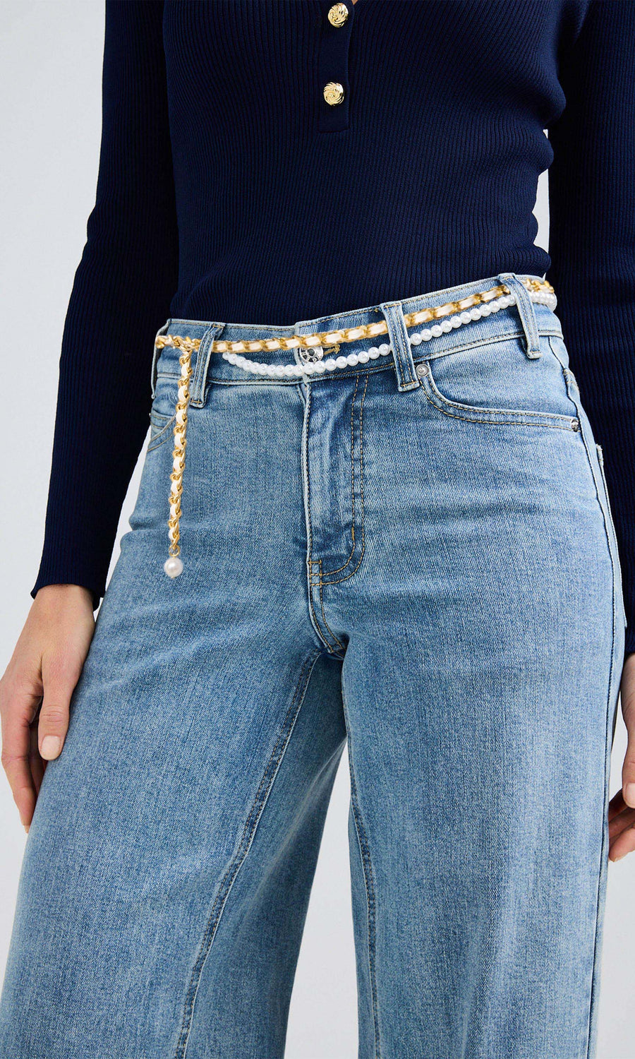 Close-up of a woman wearing a blue sweater and denim jeans, highlighted by a pearl belt.