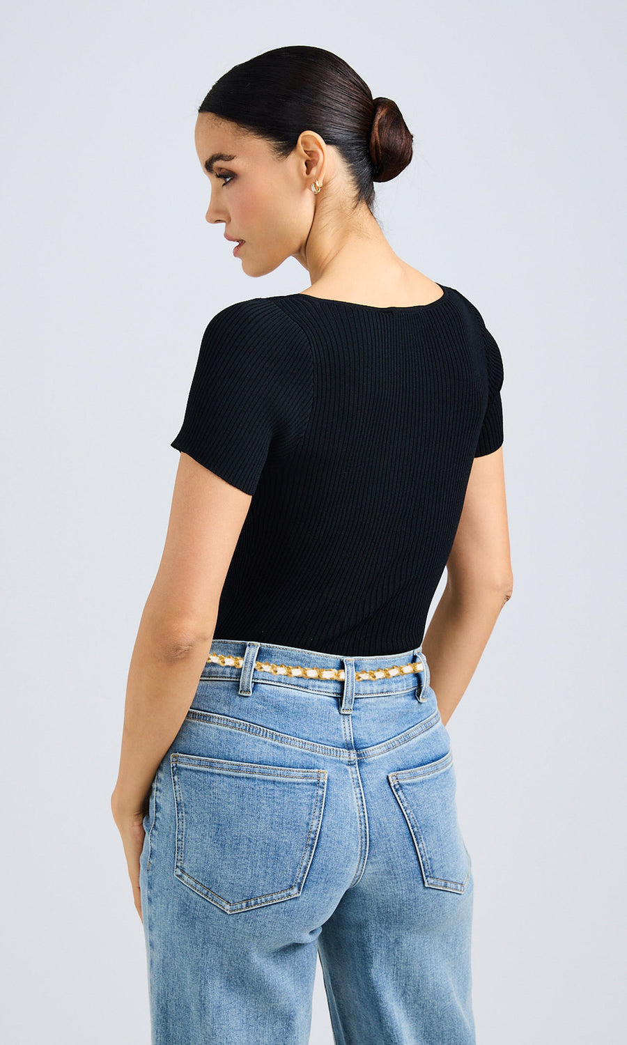 Rear view of a woman dressed in jeans and a black top, highlighting her relaxed outfit.