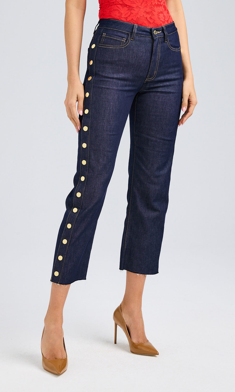 A woman wears dark denim high-rise jeans adorned with golden buttons, creating a fashionable and eye-catching outfit.