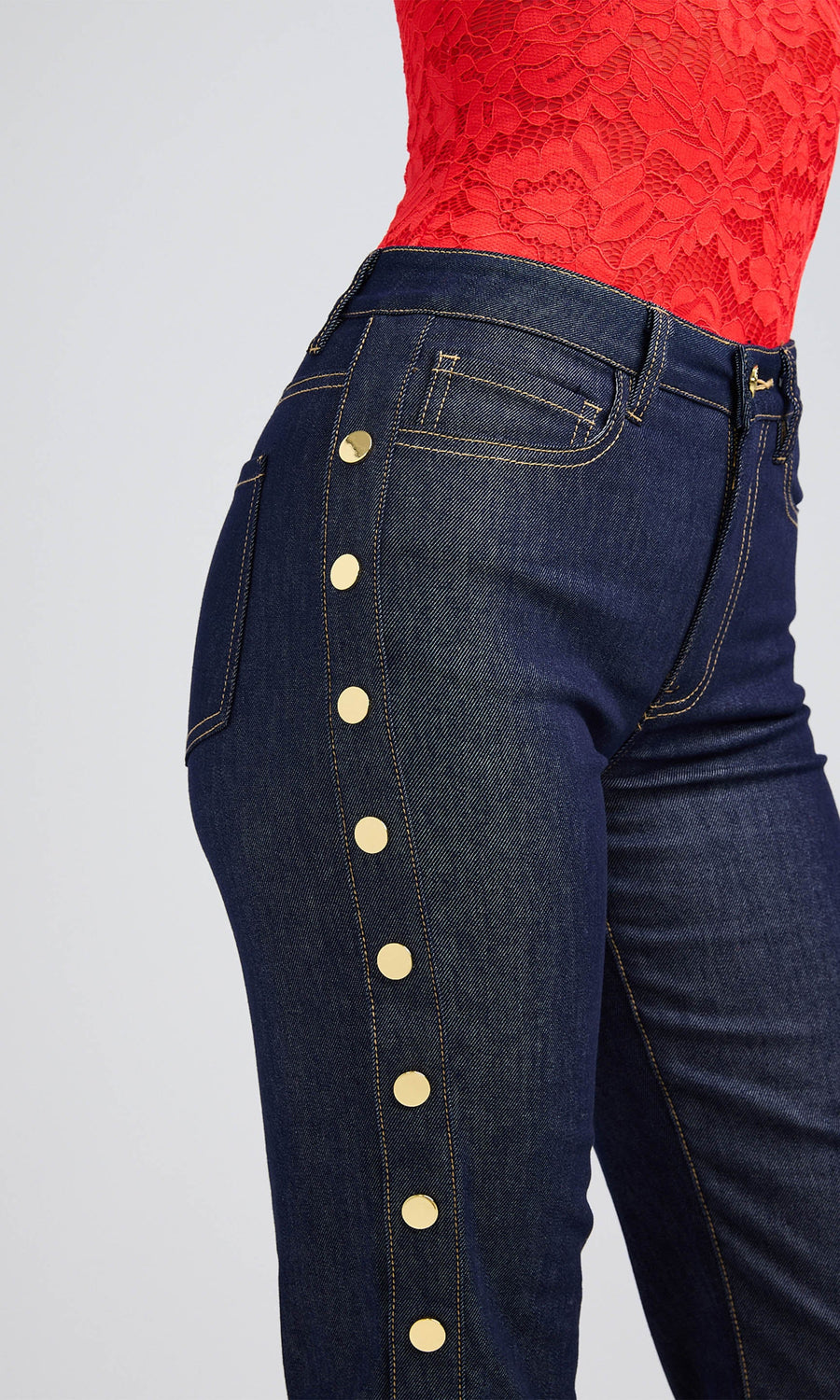 Close-up of dark denim jeans with gold buttons, worn by a woman in a red top.