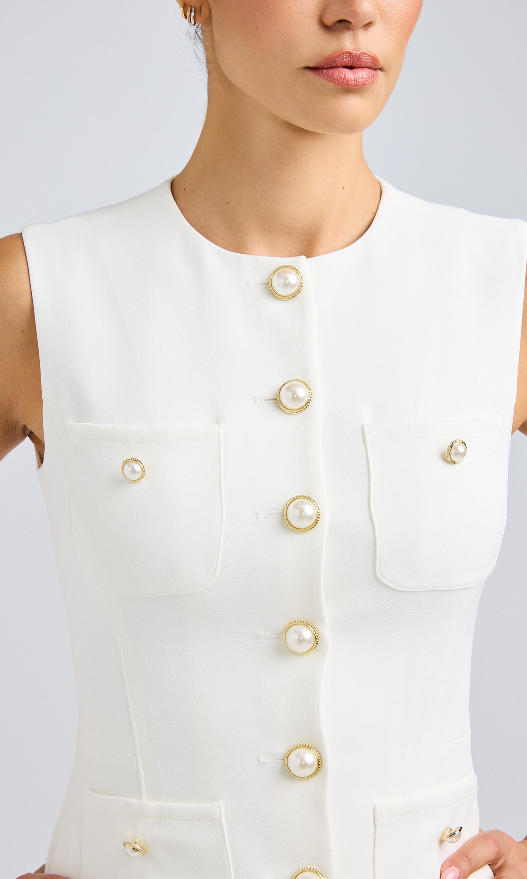 Close-up of a woman wearing a white crepe blouse, featuring stylish pearl and gold buttons for a chic look.