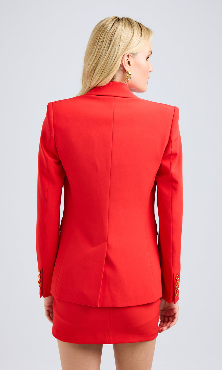 Rear view of a woman in a red blazer featuring gold button details, highlighting her fashionable look.