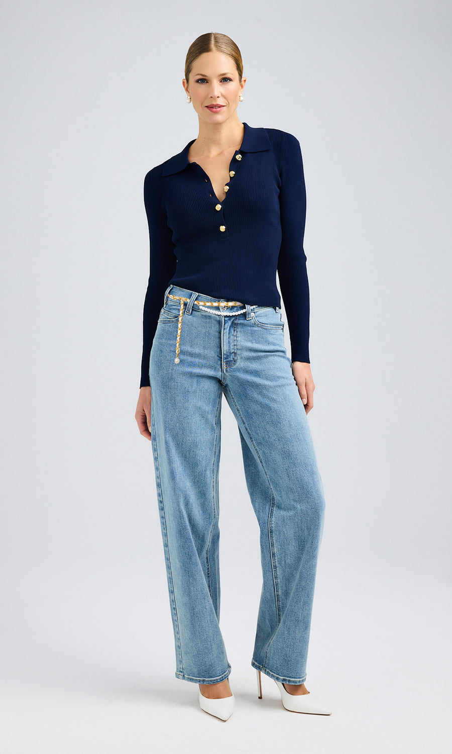 Model stands confidently in a navy sweater and bahama blue jeans, showcasing a pearl belt that adds elegance to the casual look.