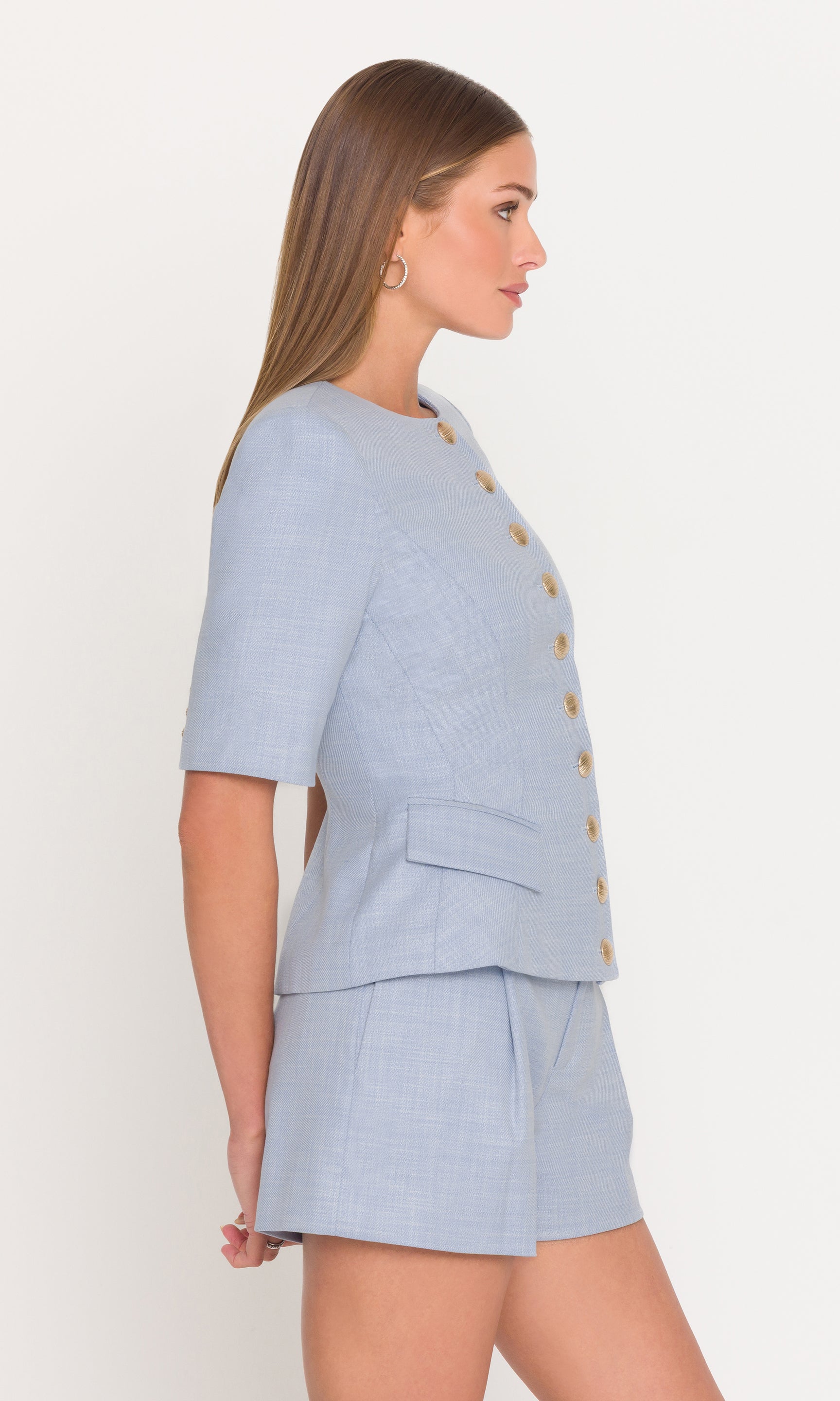Model wears the Adriana Chambray Suiting Jacket in chambray blue in a side view, showing the peplum flare and fitted silhouette.