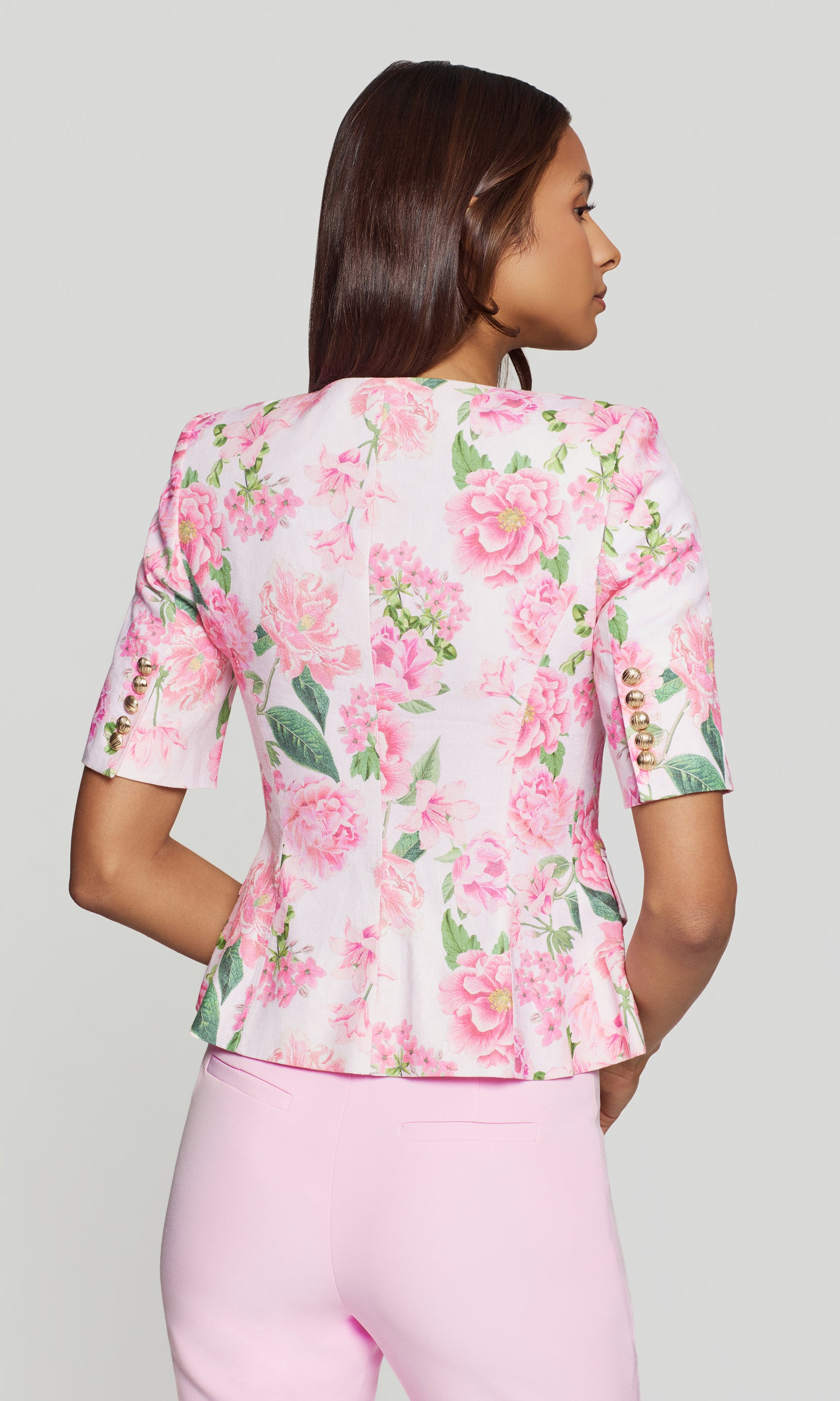 Back view of woman wearing a pink floral blouse and pink pants on a gray background