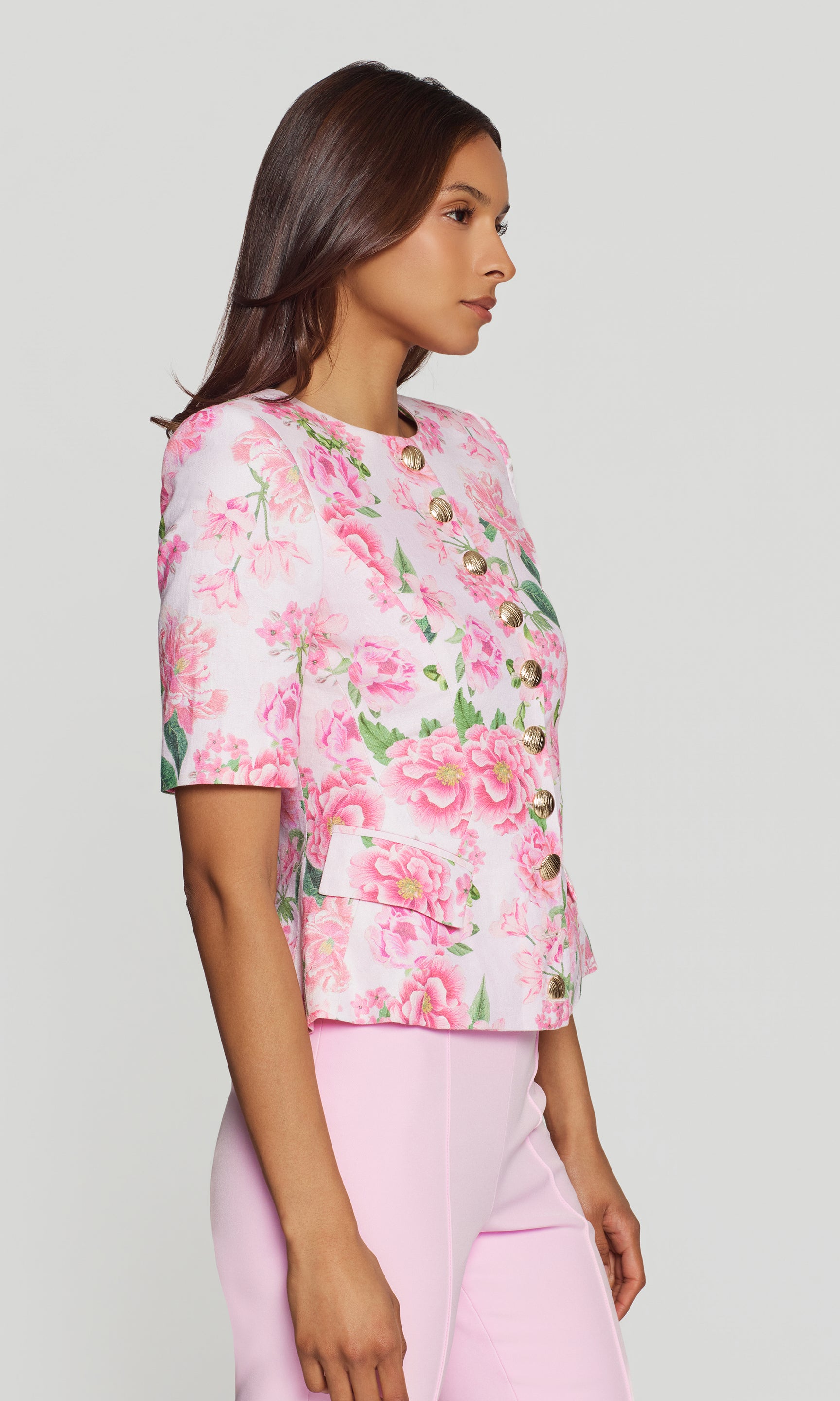 Side view of woman wearing a pink floral jacket and pink pants on a light gray background