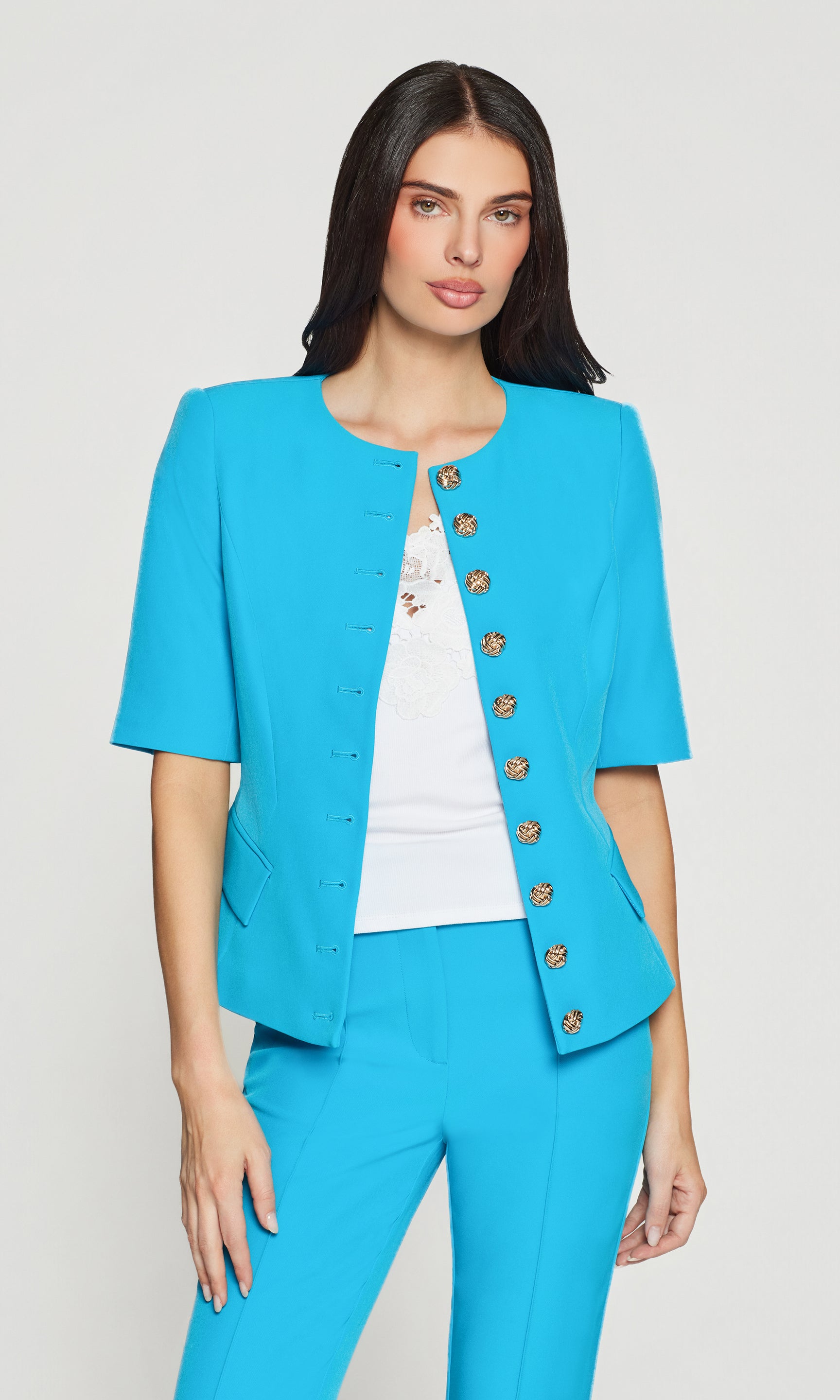 Woman wearing a turquoise suit with a white top on a light gray background