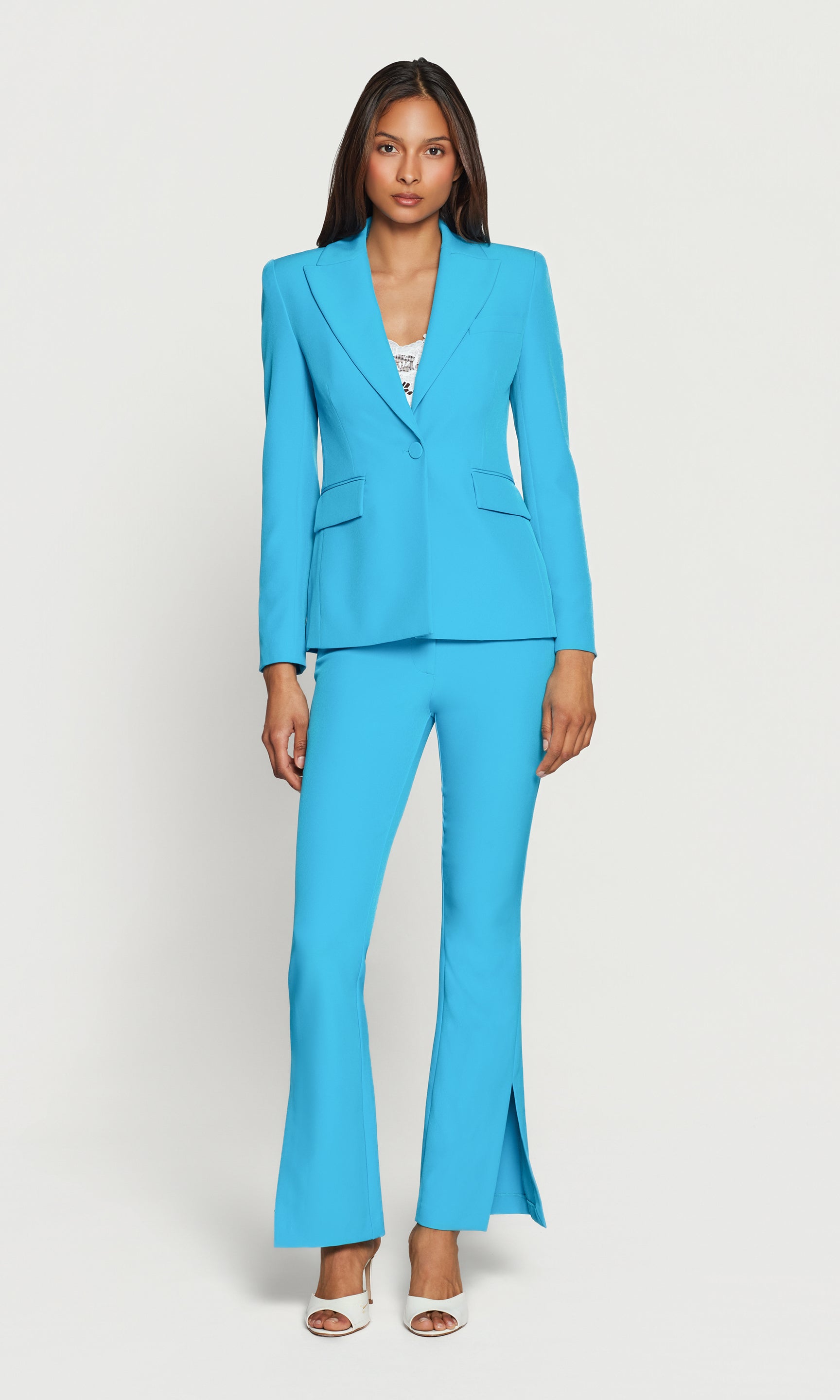 Woman wearing a bright blue suit wit white heels on a white background