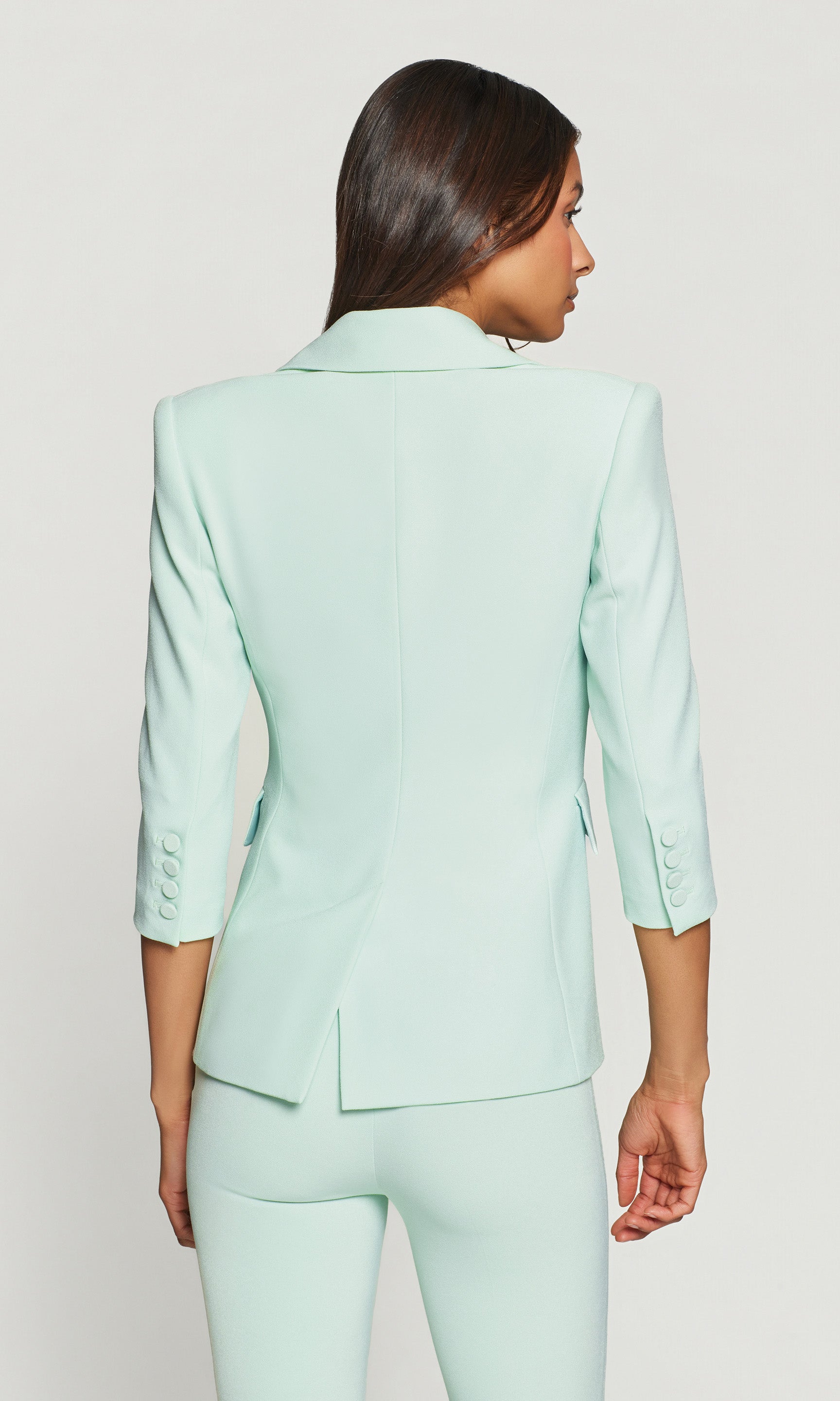 Back view of woman wearing a light green suit on a plain background
