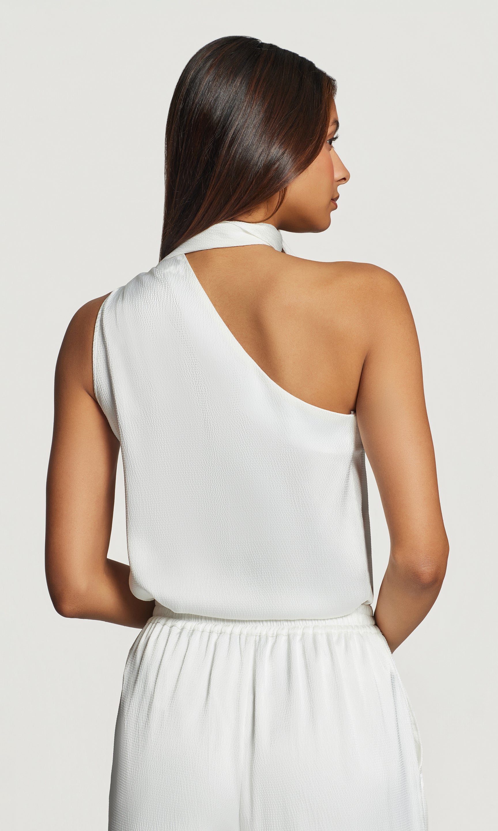 Back view of woman wearing a white one-shoulder blouse against a plain background
