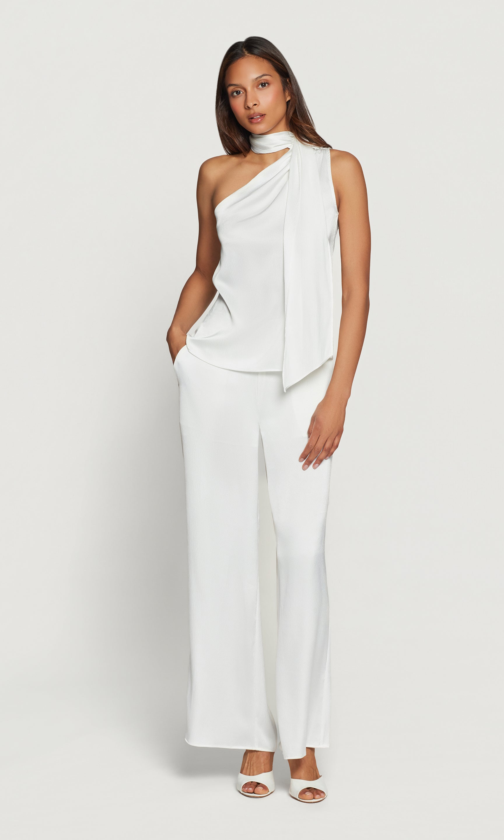 Woman wearing a white one-shoulder blouse and pants on a light gray background