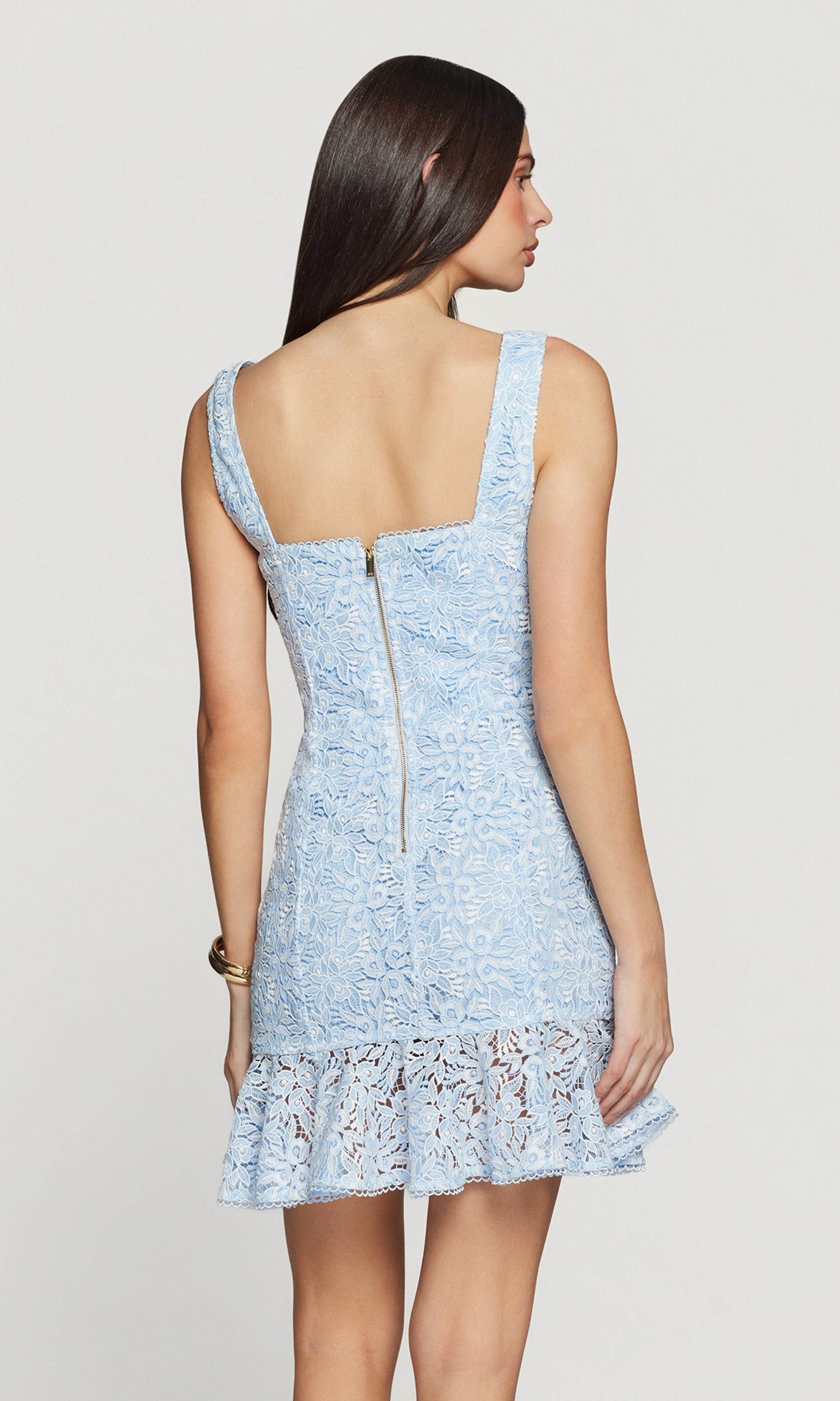 Back view of woman wearing a light blue lace dress on a plain background